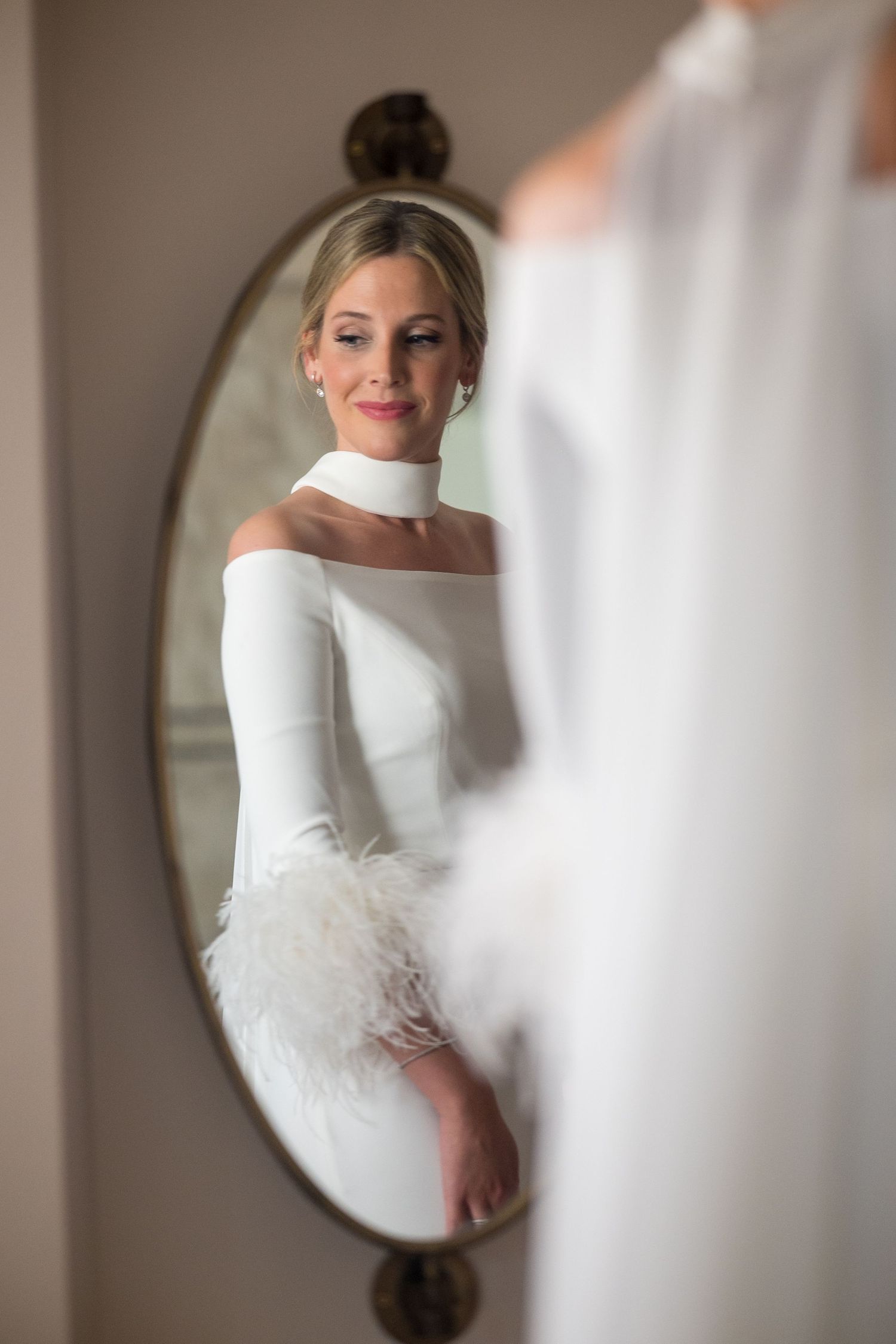 Elegant bride in a strapless white wedding dress reflected in circular mirrors during preparation.
