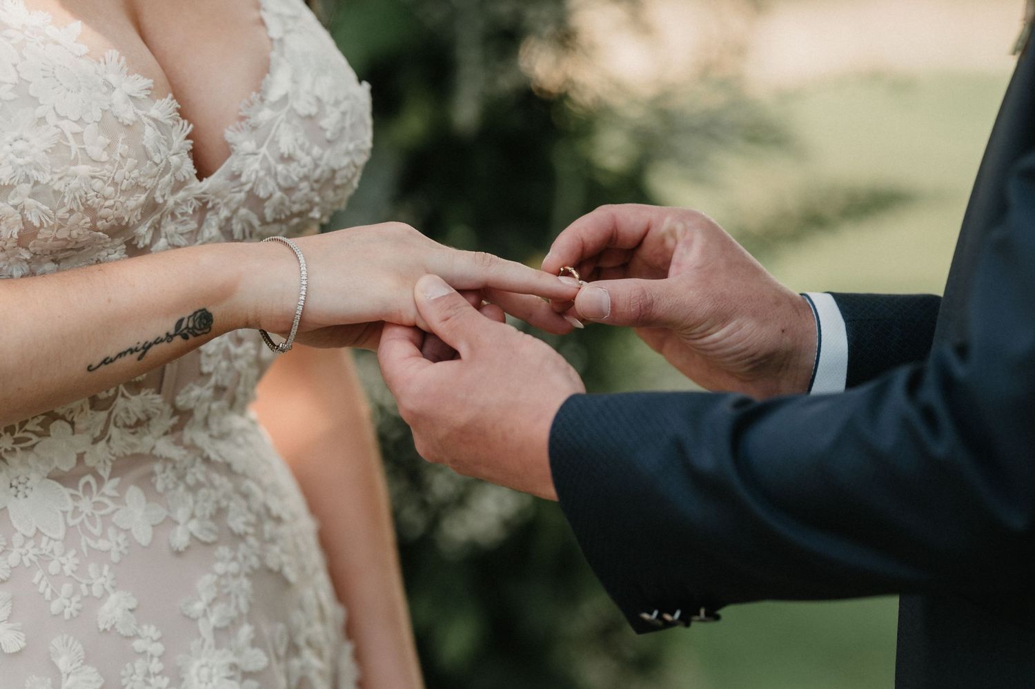 Close-up of hands exchanging wedding rings during an outdoor ceremony.