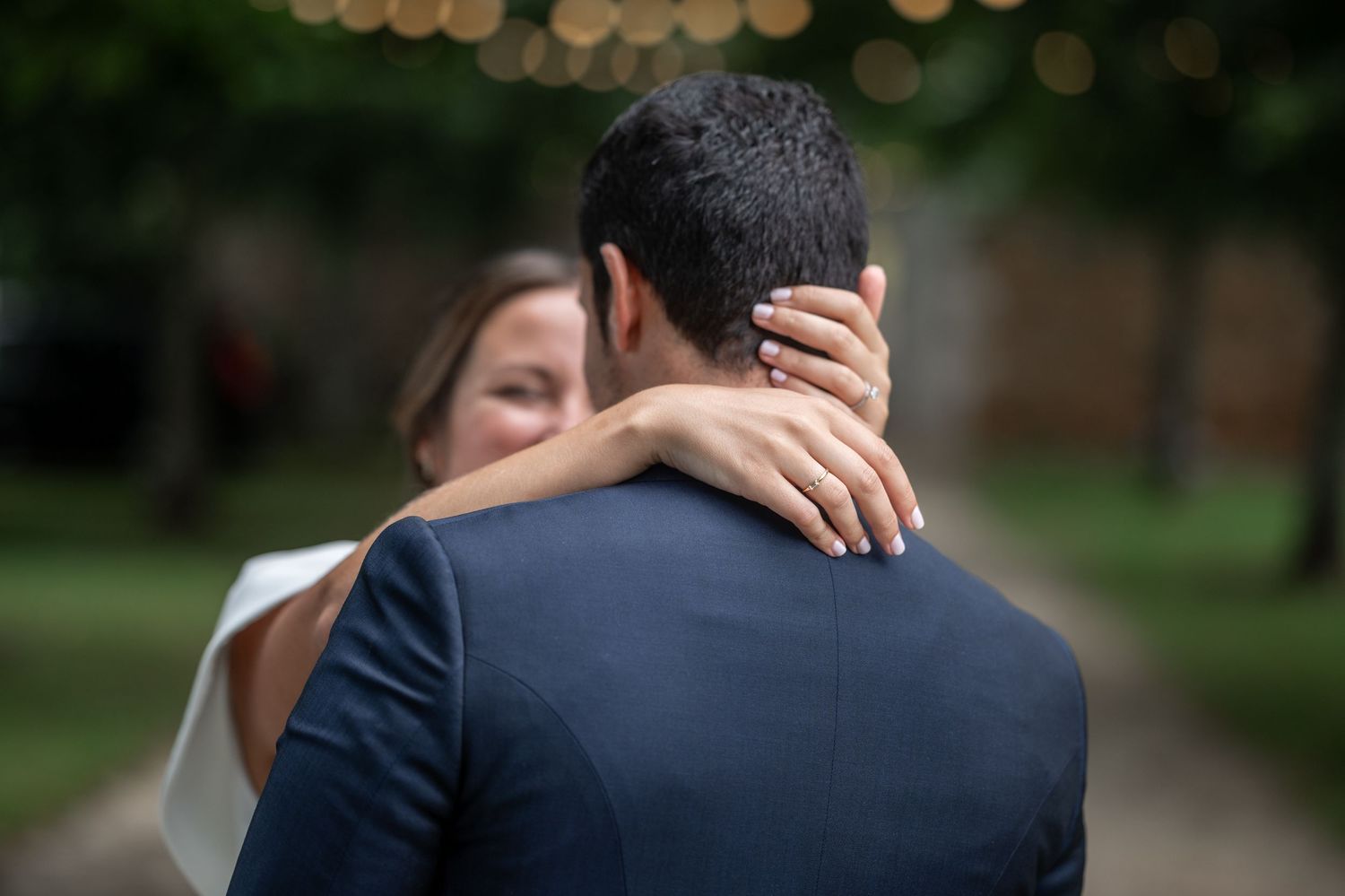 A romantic couple embraces during their wedding celebration under hanging string lights and paper lanterns.