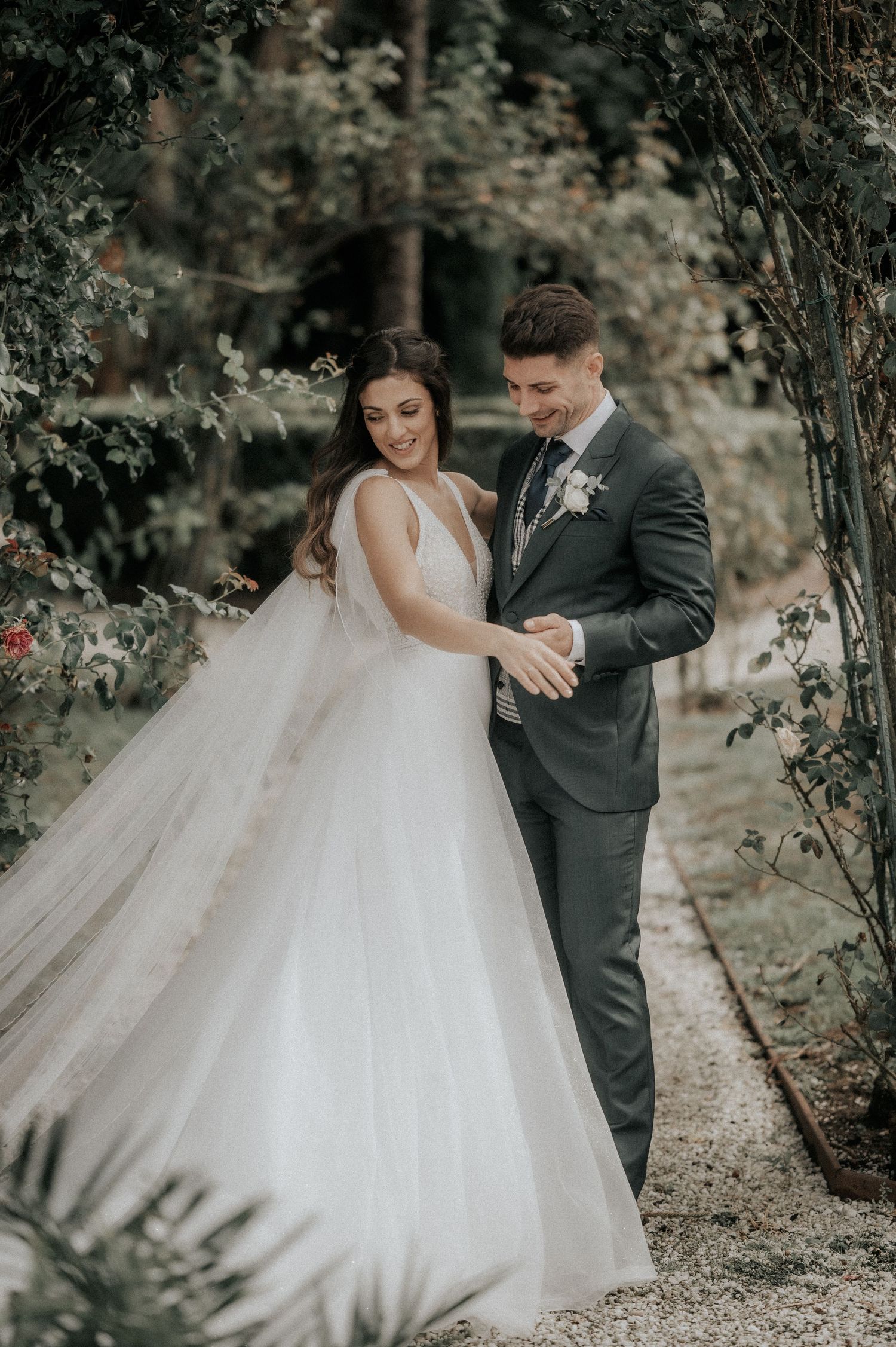 A romantic wedding couple shares a joyful moment on a garden path surrounded by lush greenery.