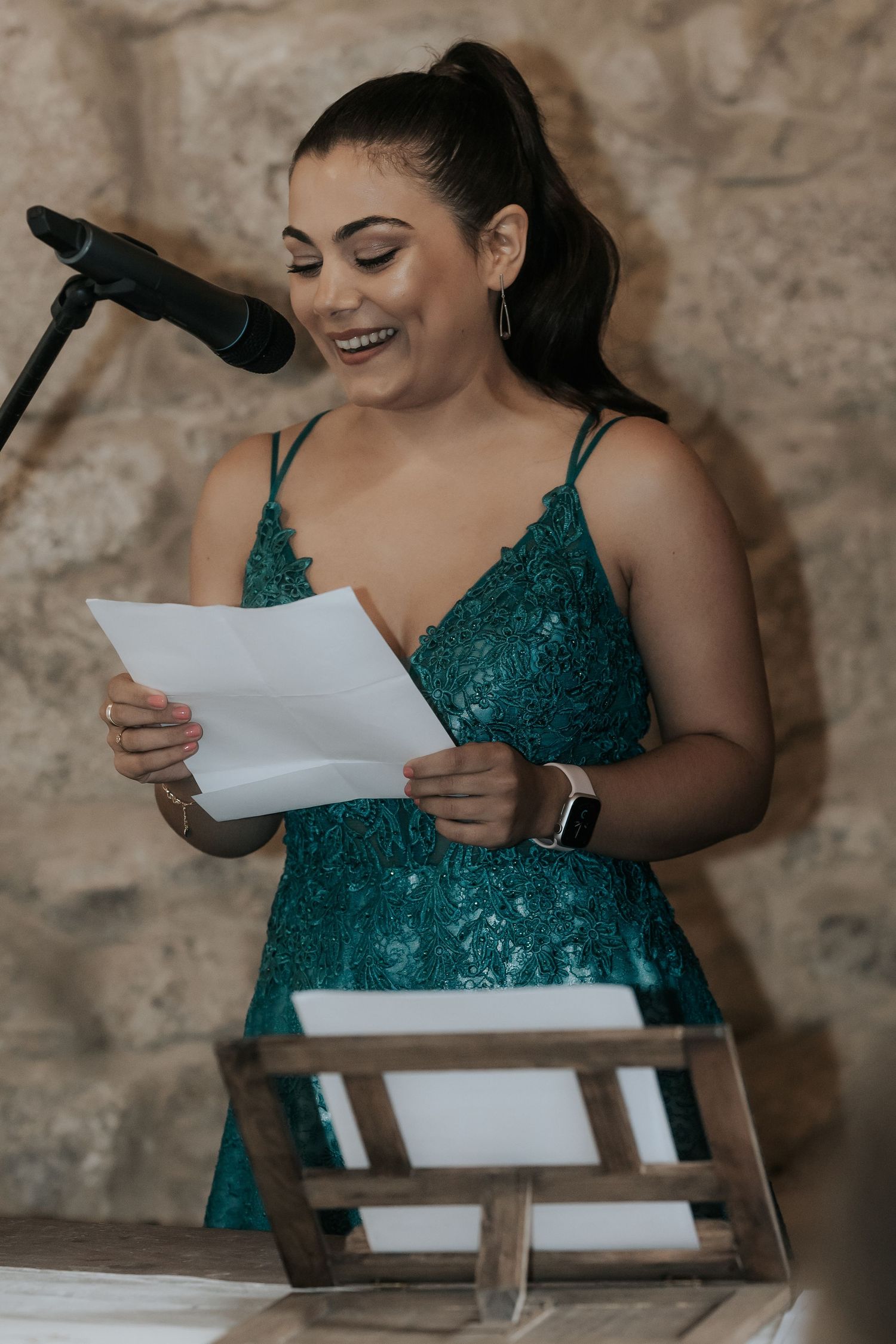 A speaker in a sparkling emerald green dress smiles while reading from papers at a podium during an event.