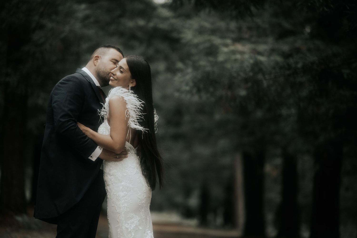 A romantic couple shares a tender kiss in a moody forest setting with dramatic lighting and shadows.