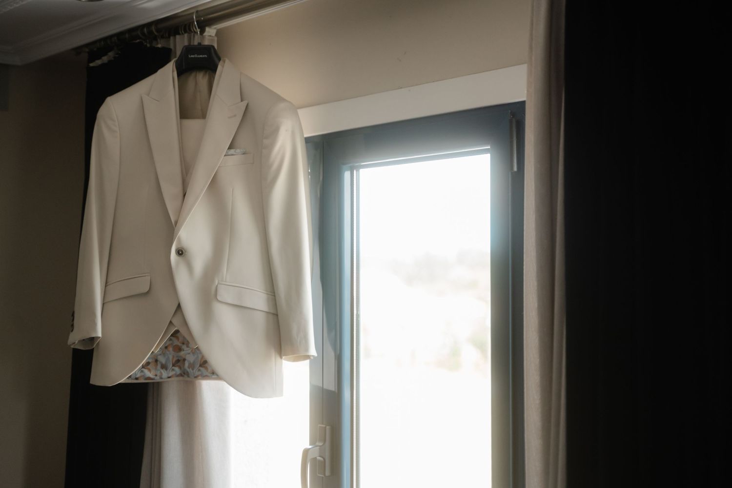A white bathrobe hangs on a door hook near a bright window in a minimalist interior setting.