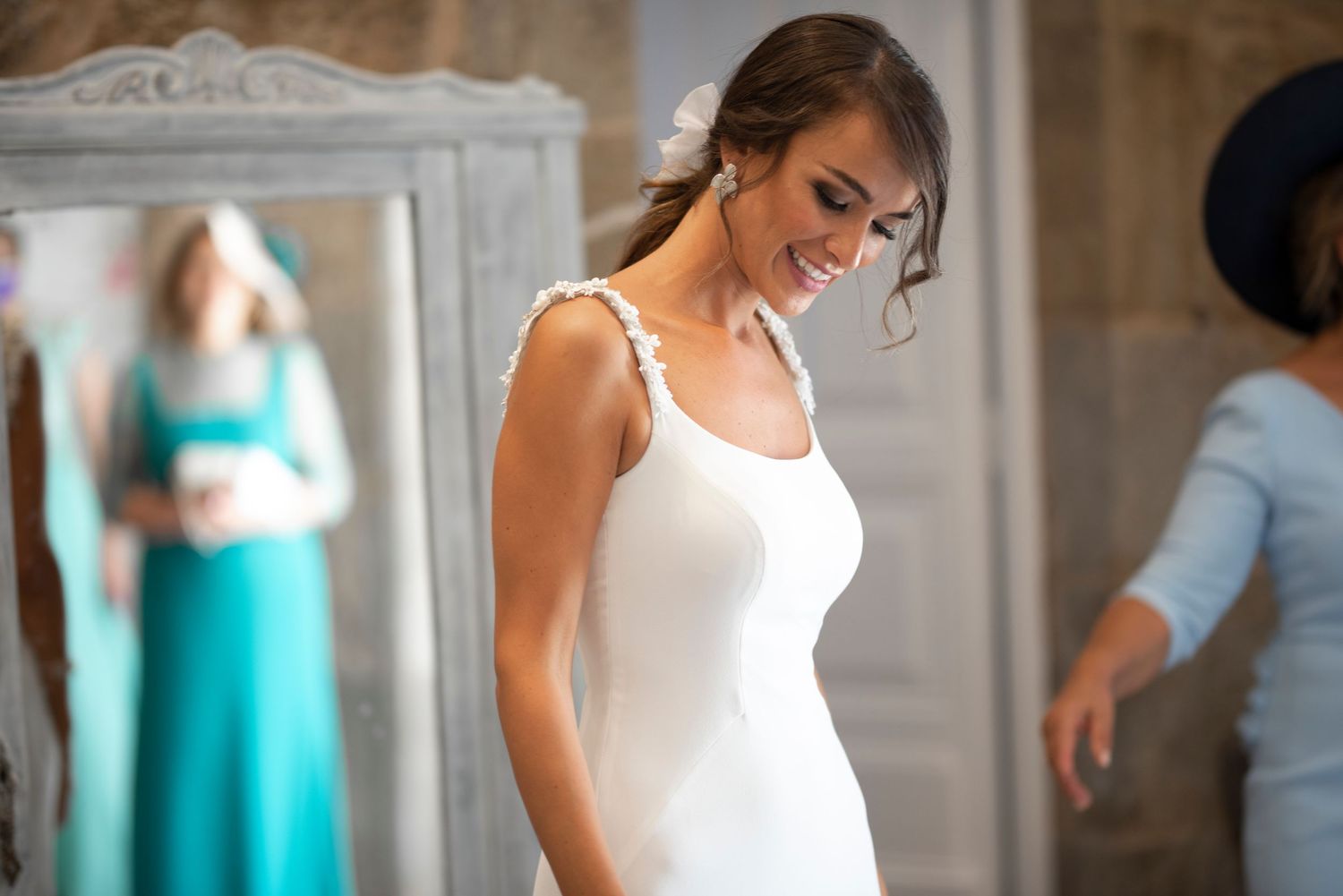 Bride in sleeveless white gown preparing with bridesmaids in turquoise dresses.