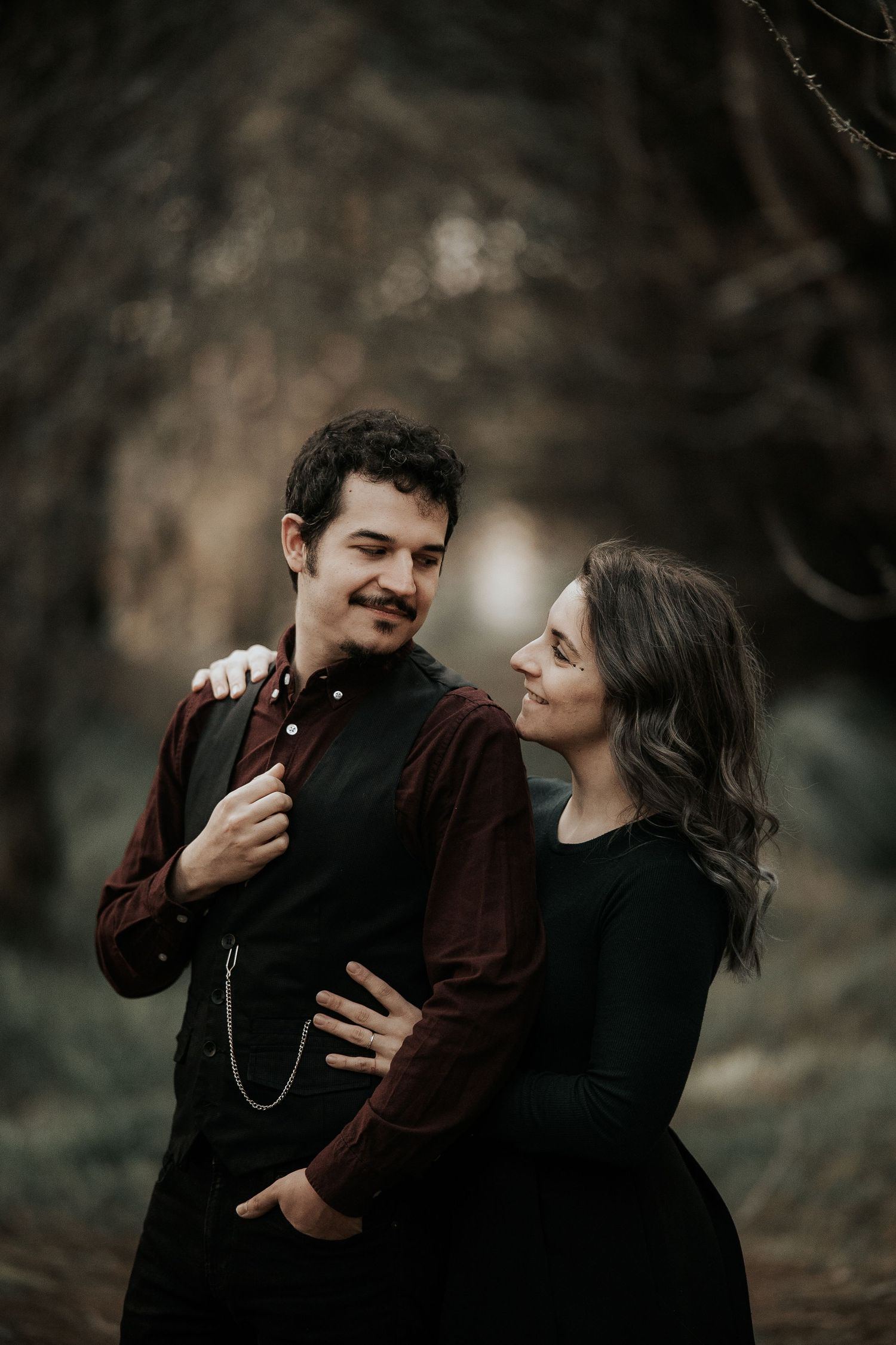 A romantic couple in dark clothing shares intimate moments in a moody outdoor setting.