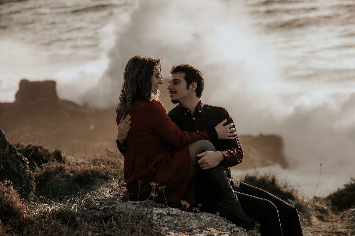 A couple embraces against a dramatic cloudy sky in a romantic outdoor photoshoot.