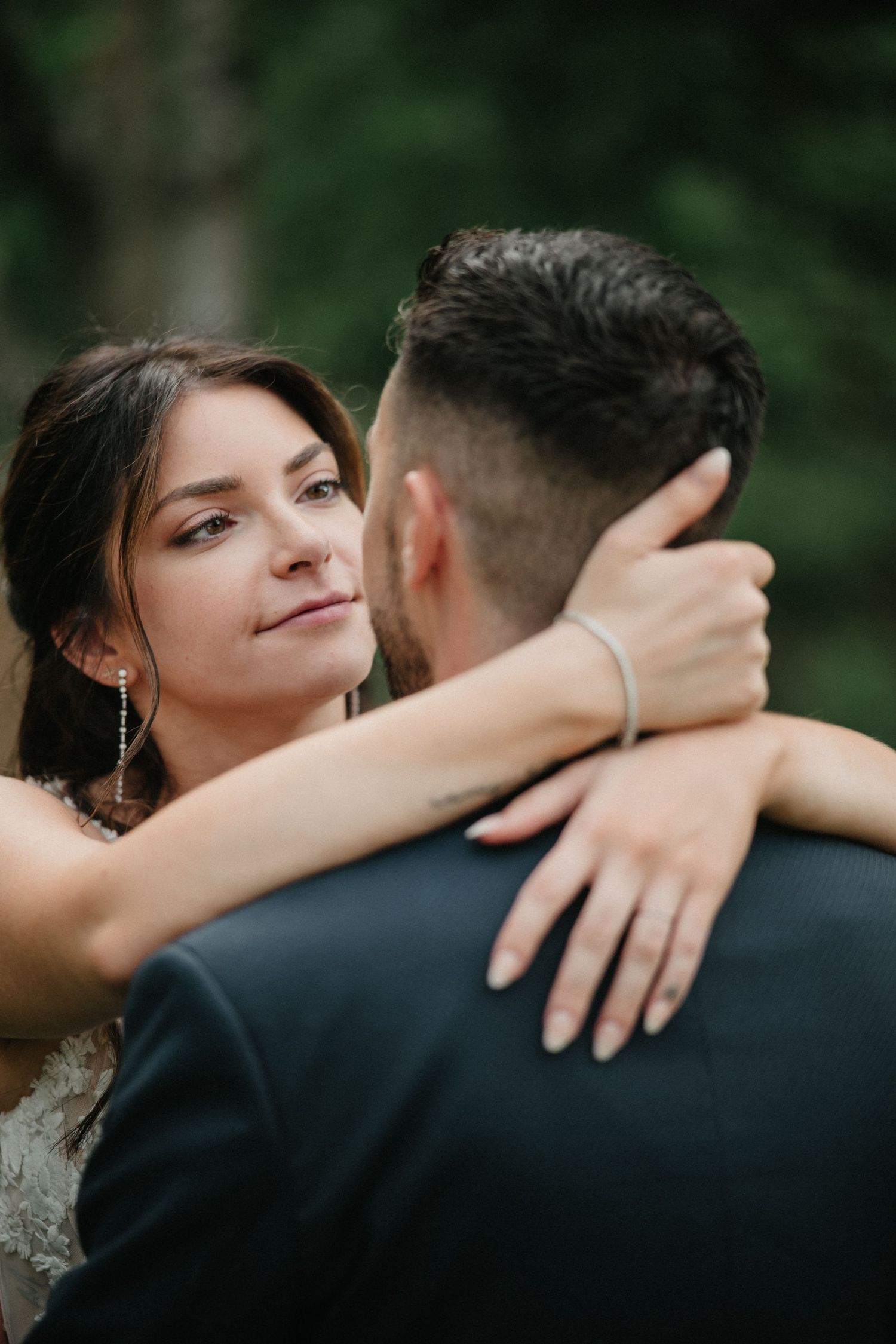 A romantic couple embraces outdoors in a natural setting with soft lighting and greenery in the background.