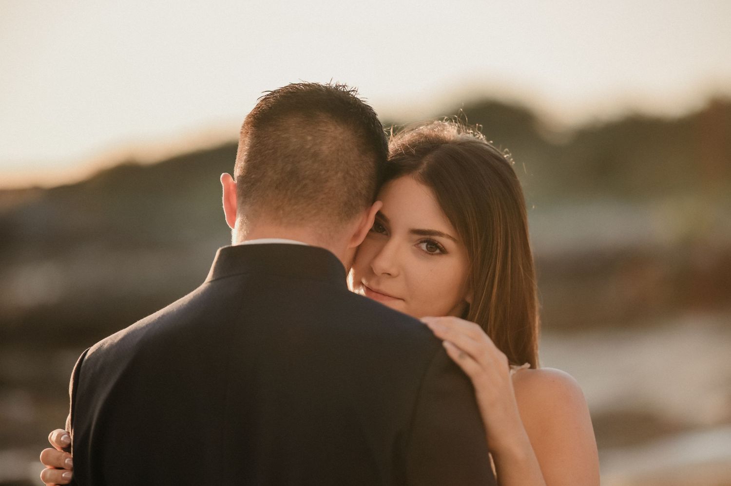 A couple embraces during sunset at a scenic outdoor location creating a romantic silhouette against the golden sky.
