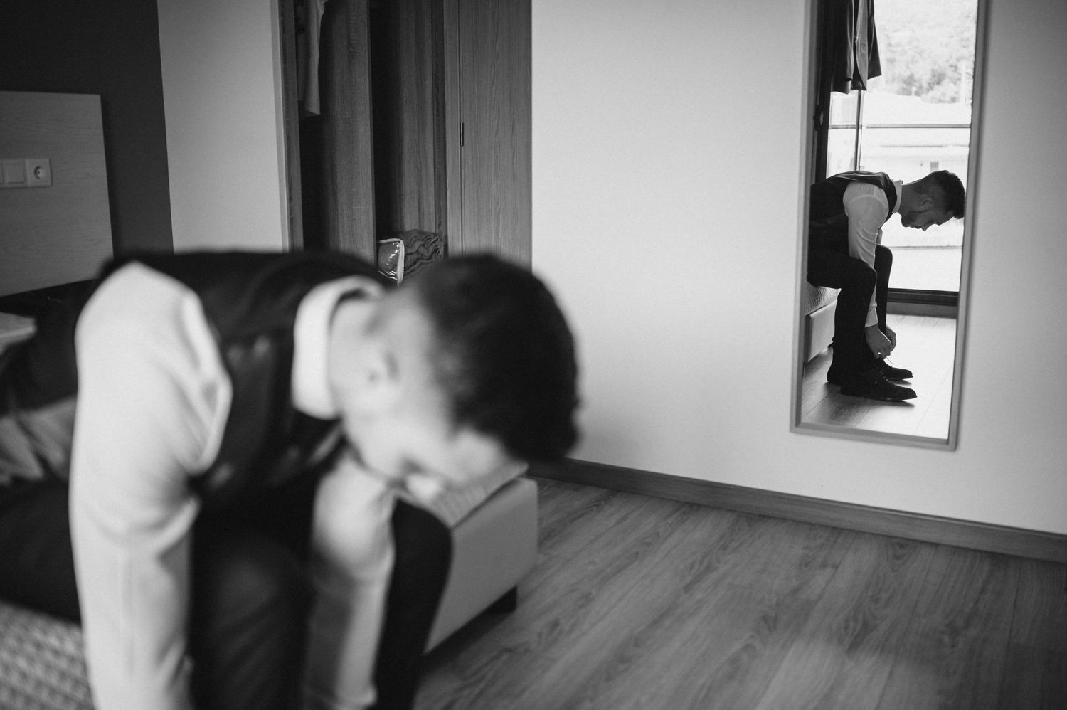 A black and white photograph shows a person lying on a hardwood floor next to a window.