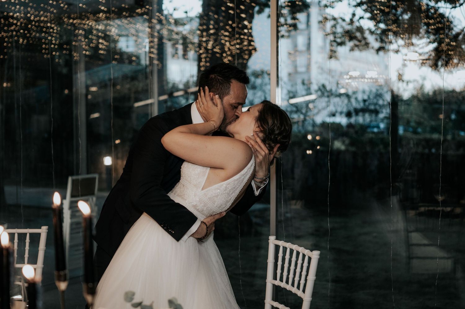 Romantic couple shares an intimate dance moment at an evening wedding reception with twinkling lights in background.