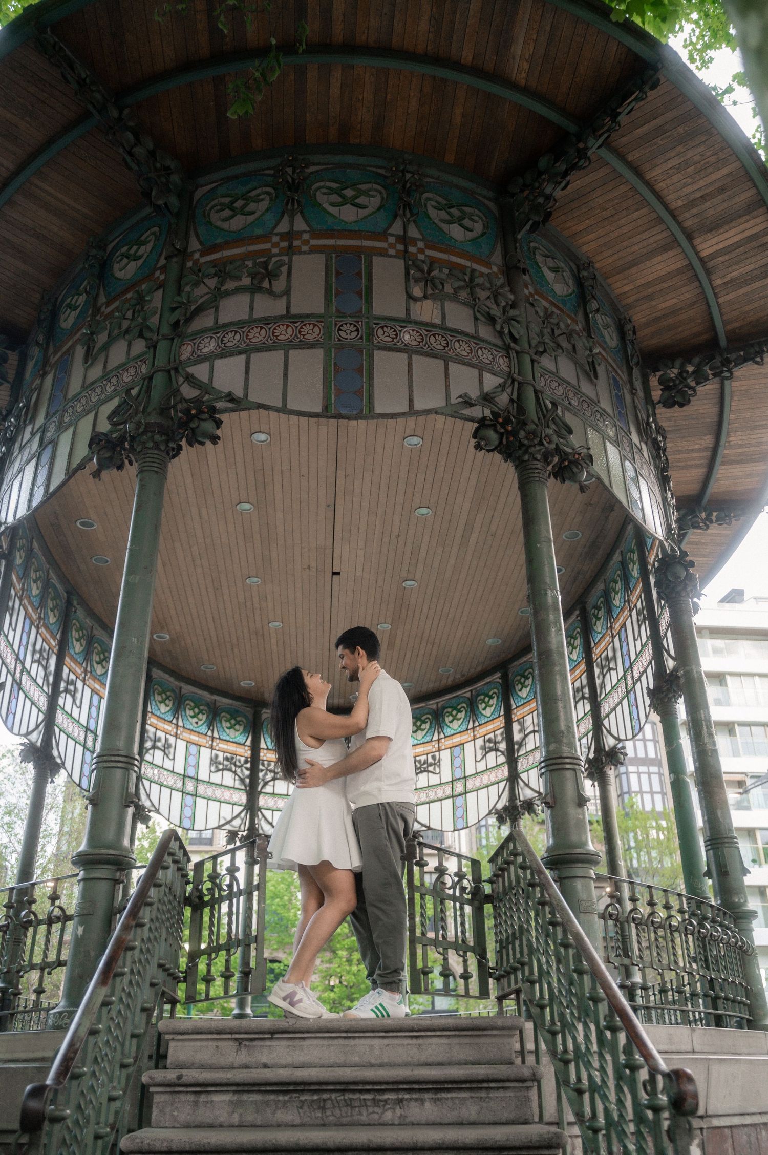 Ornate vintage gazebo with decorative ironwork and curved roof in a garden setting.