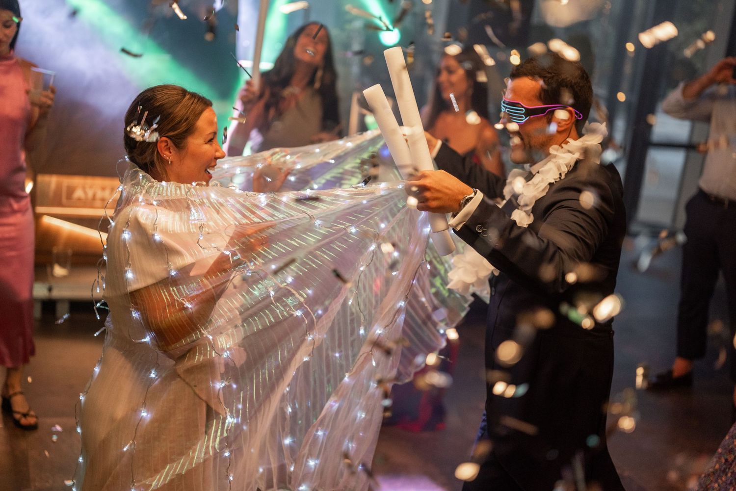 People dancing and celebrating at a wedding reception with confetti and bubbles floating through the air.
