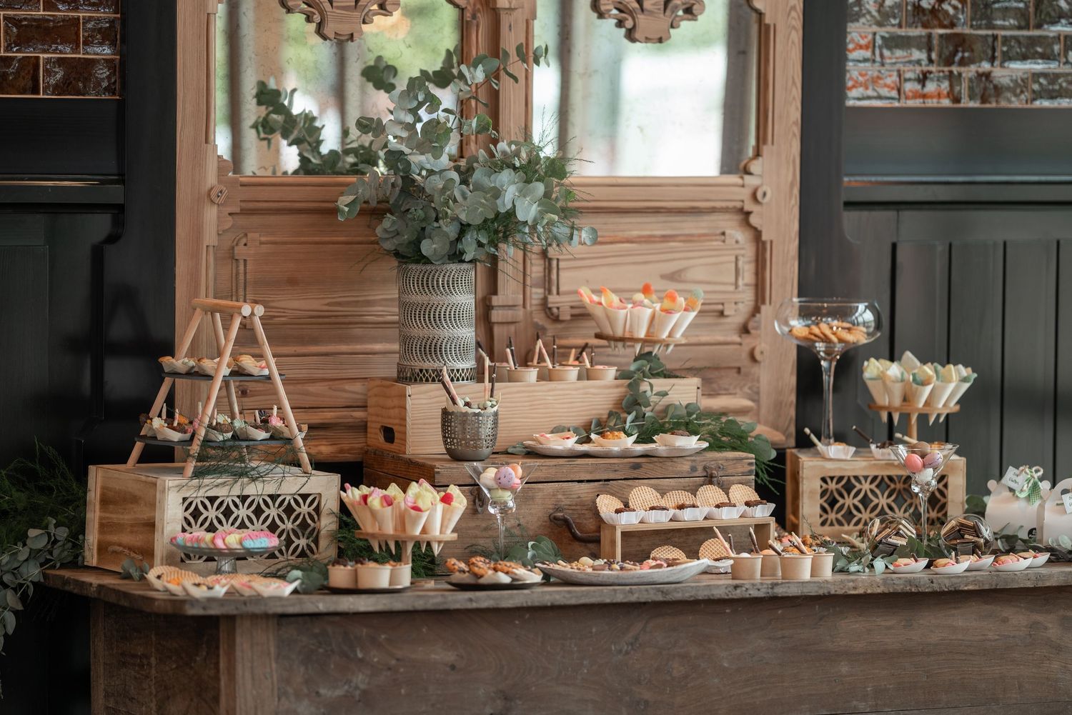 Rustic dessert table display with wooden crates, eucalyptus garland, and tiered stands holding treats at a wedding reception.