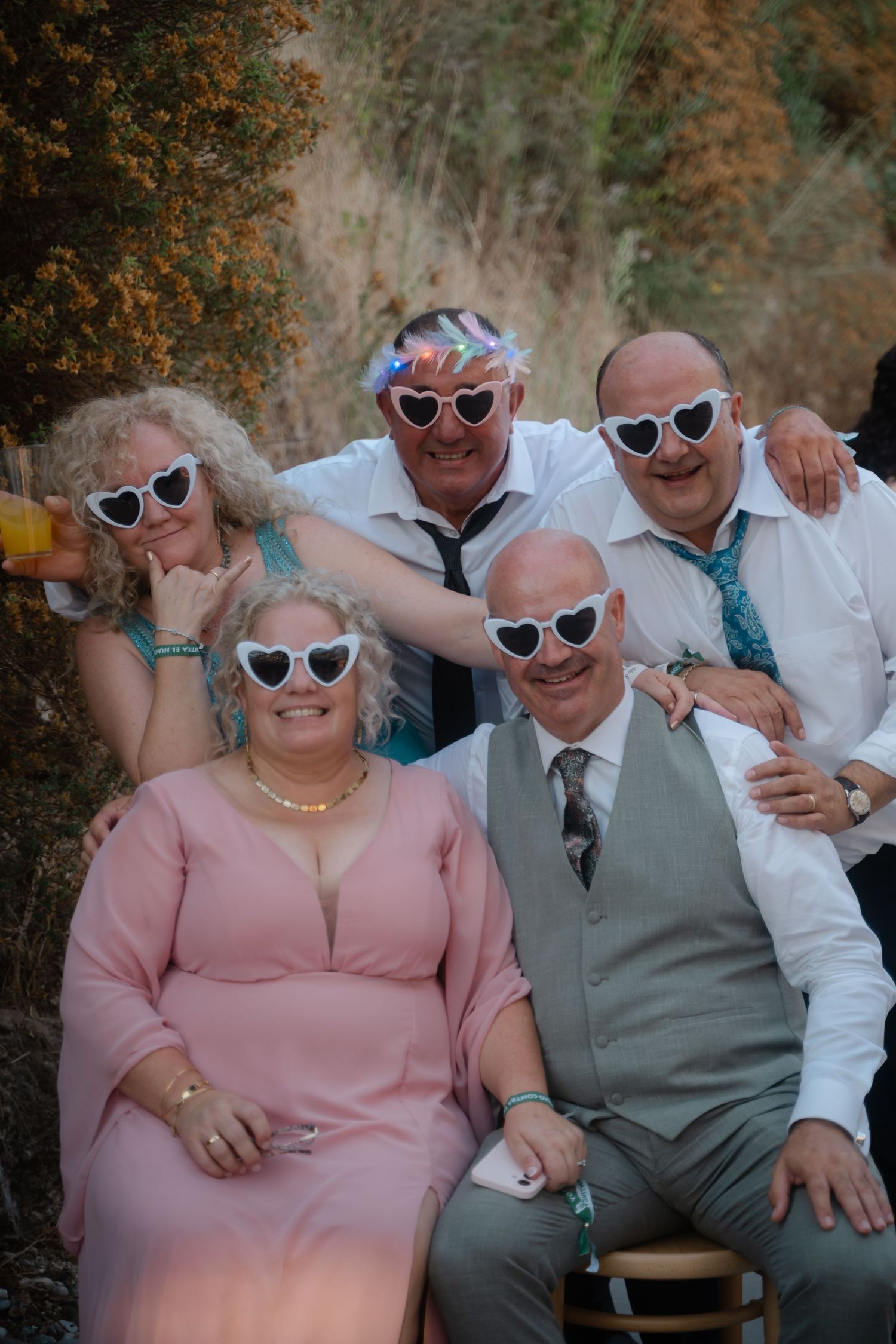 Wedding party members wearing retro sunglasses pose together outdoors.