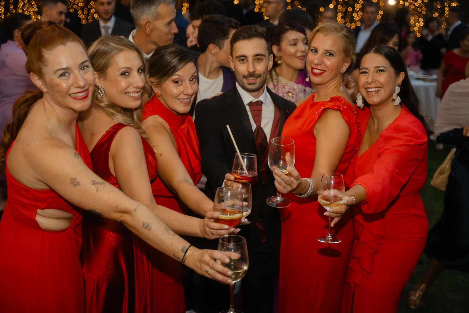 A festive celebration with guests in red dresses holding champagne glasses against a backdrop of twinkling lights.