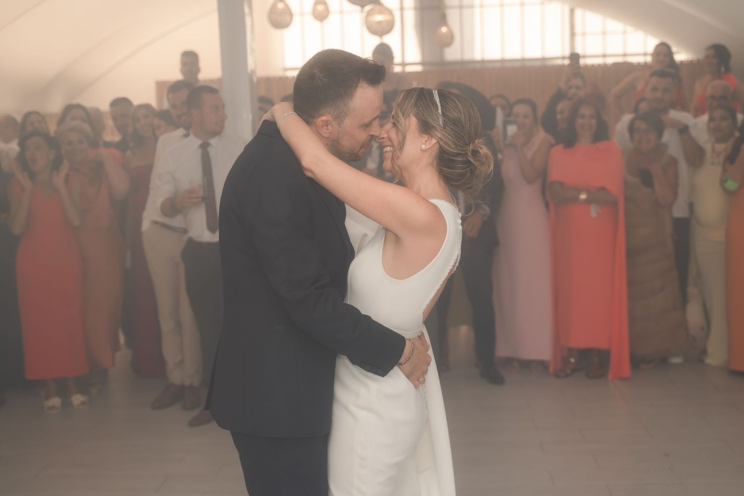 A couple performs their first dance at a wedding reception while guests watch and capture photos on their phones.