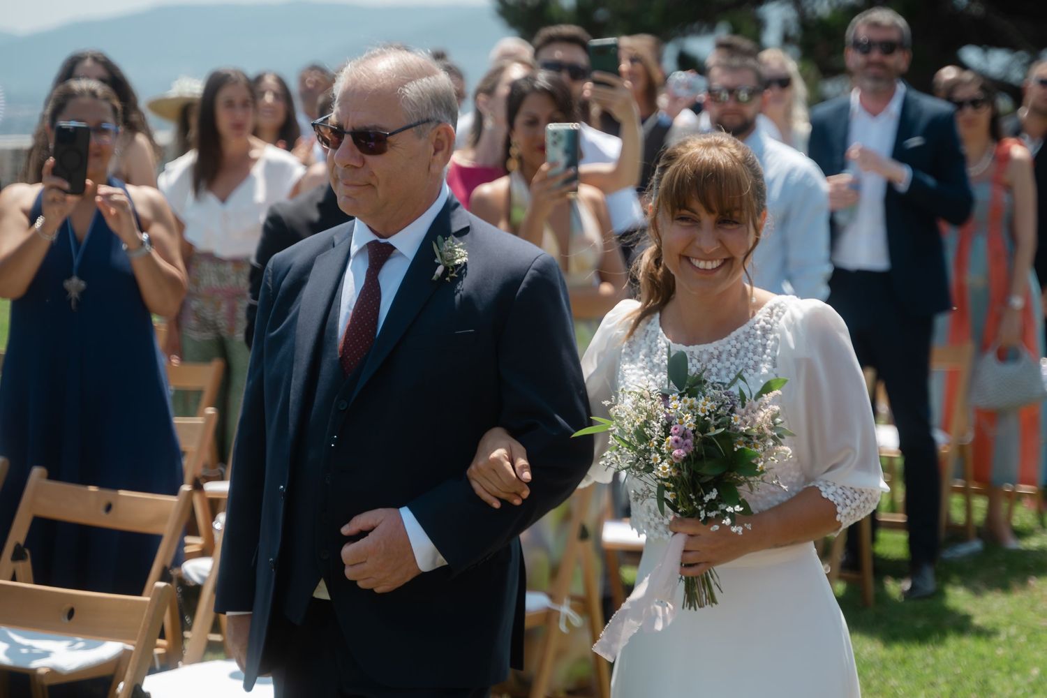 A happy couple walks down the aisle at an outdoor wedding ceremony as guests look on and celebrate.