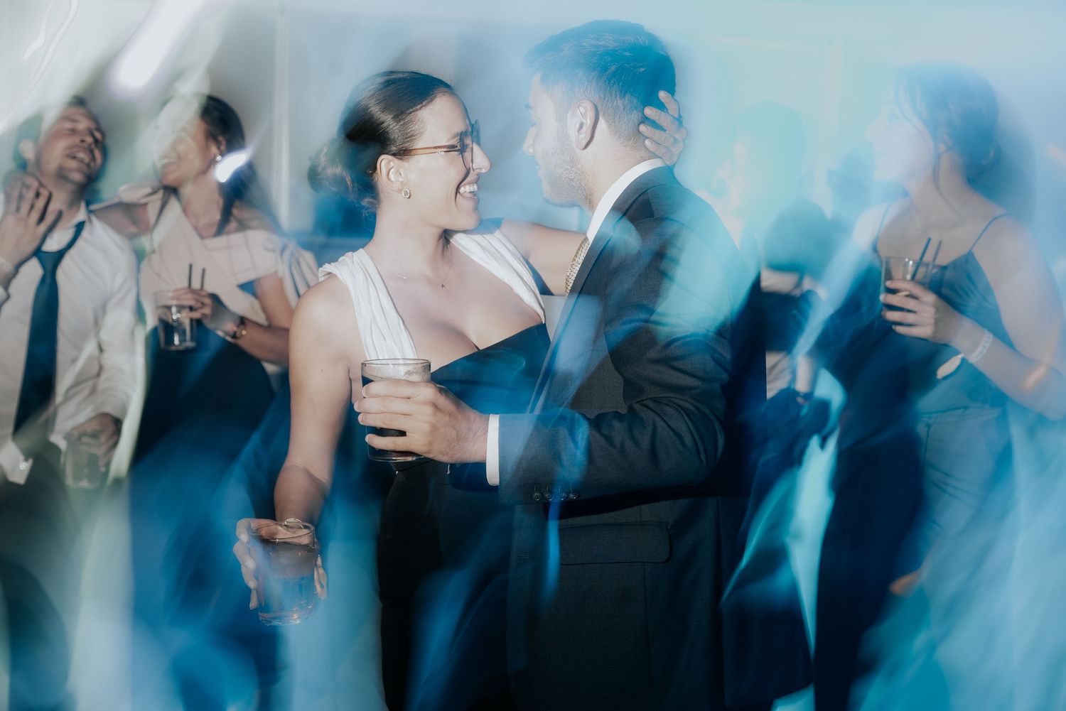 Wedding guests dance and celebrate on a dimly lit dance floor with blue lighting effects.