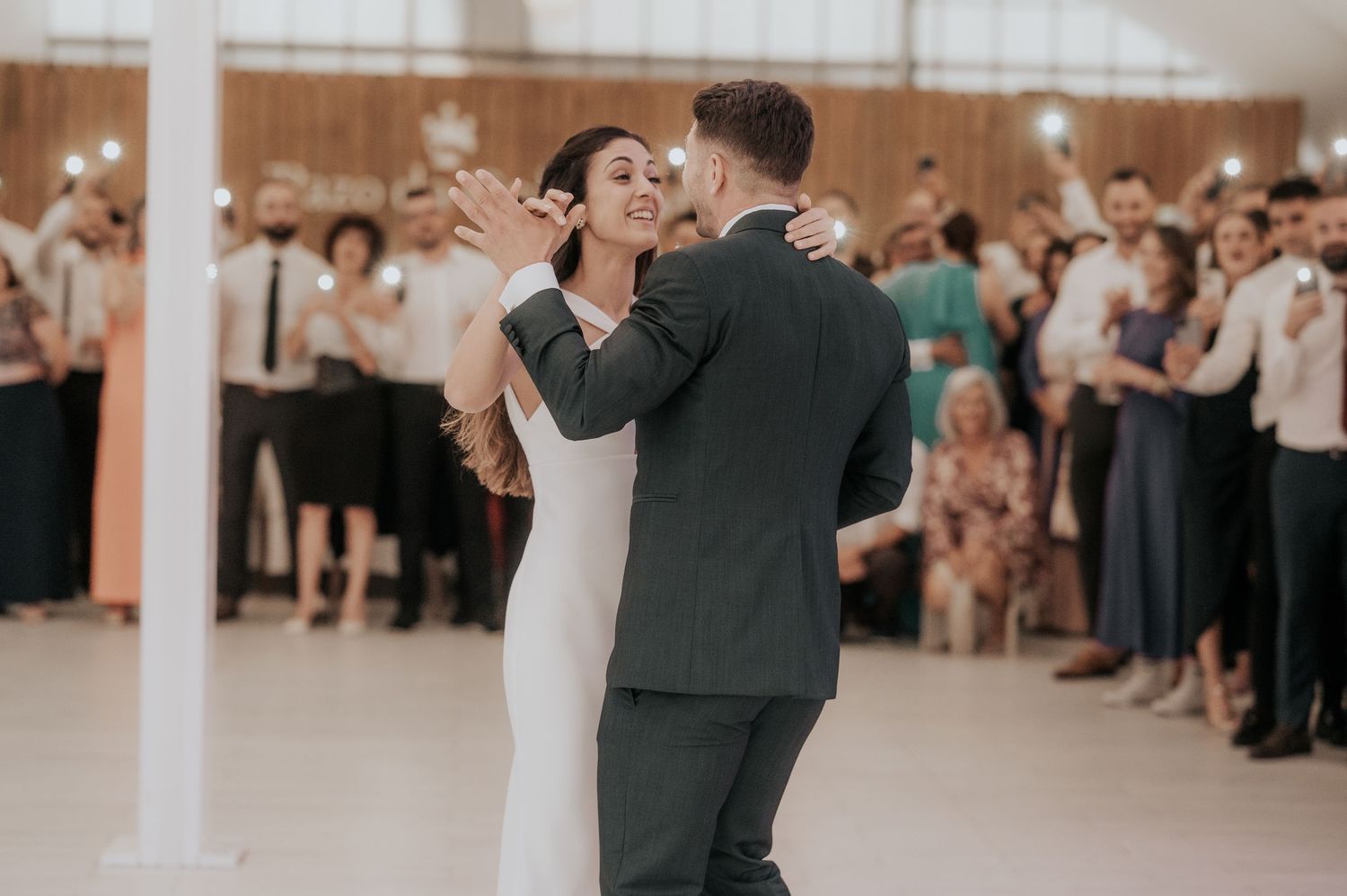 A couple shares an intimate dance during their wedding reception surrounded by guests in a bright venue.