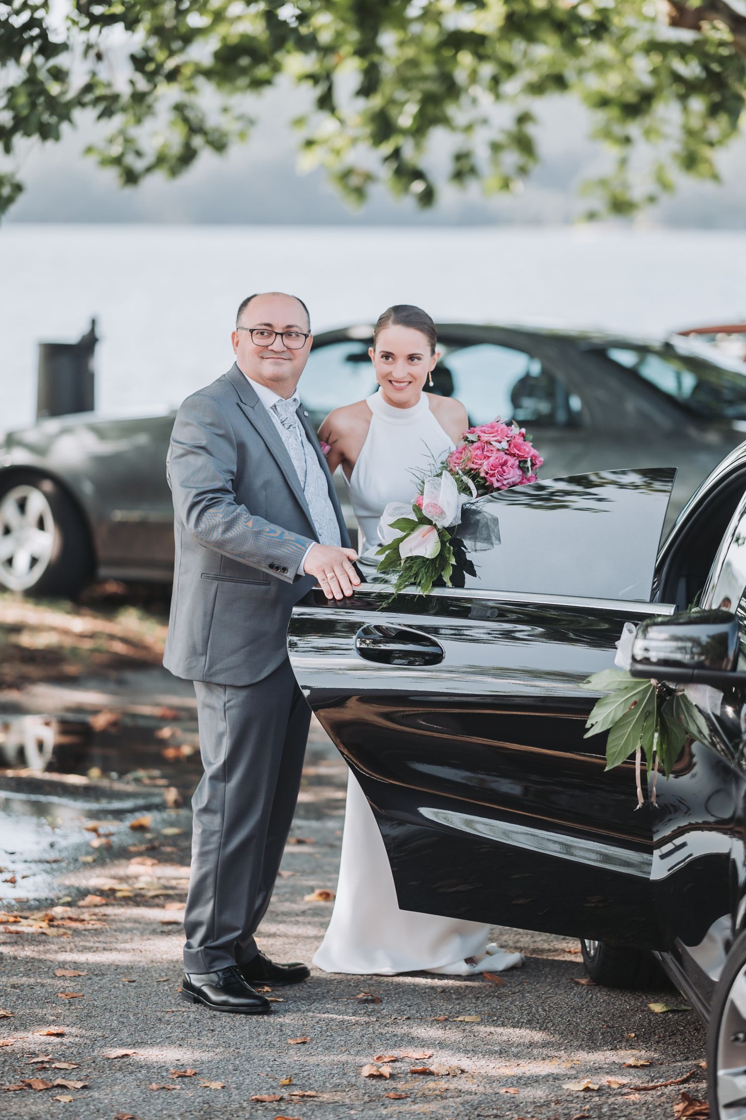 A couple poses playfully around a black grand piano outdoors during a wedding photoshoot.