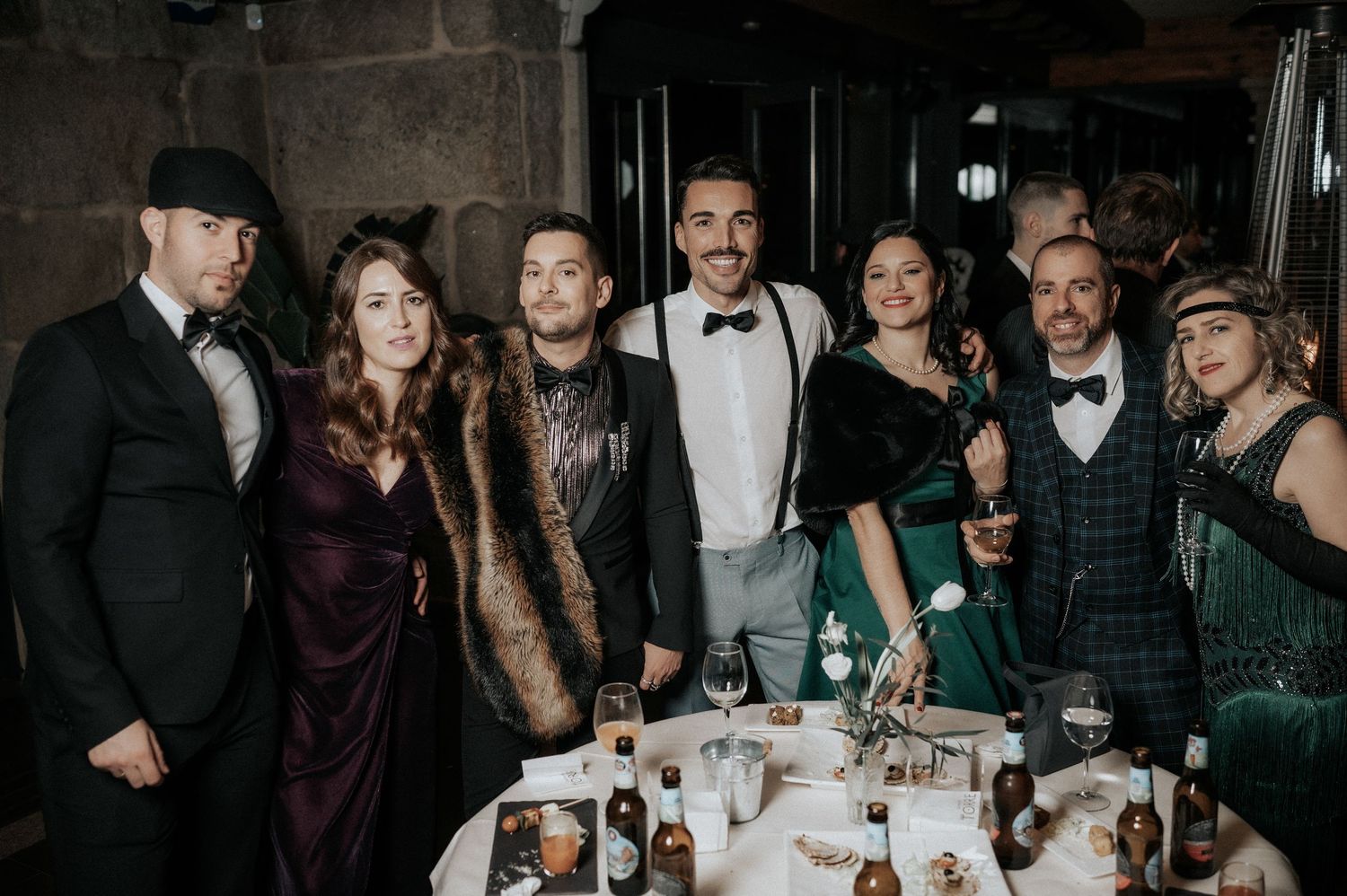 Wedding guests gather for candid group photos at an indoor reception venue with dark moody lighting.