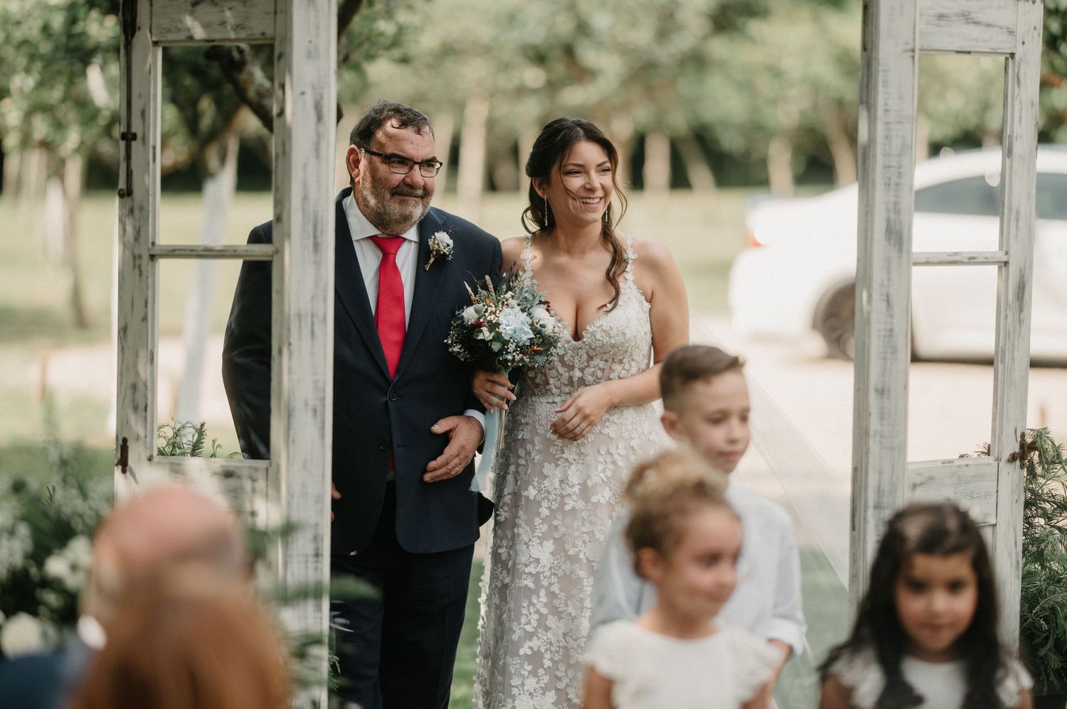 Wedding party gathered outdoors in an elegant garden setting with natural lighting and greenery.