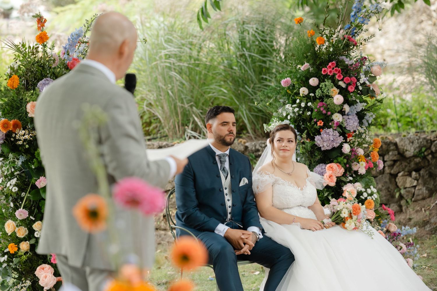 An outdoor wedding ceremony in a garden setting with colorful flowers and ornamental grasses creating a natural backdrop.