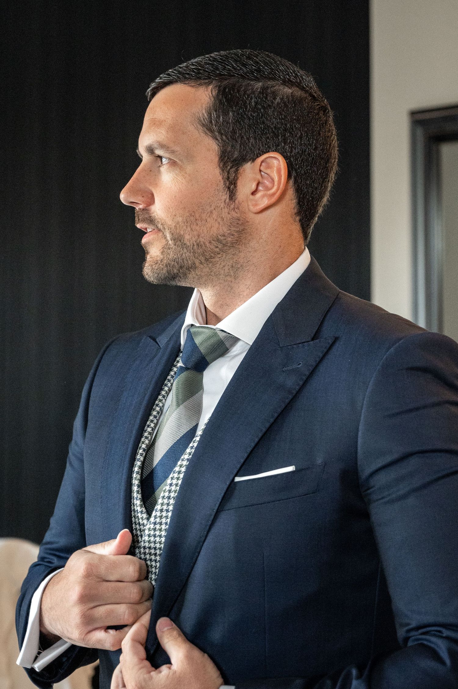Professional in navy suit adjusts his tie while getting dressed in formal business attire.