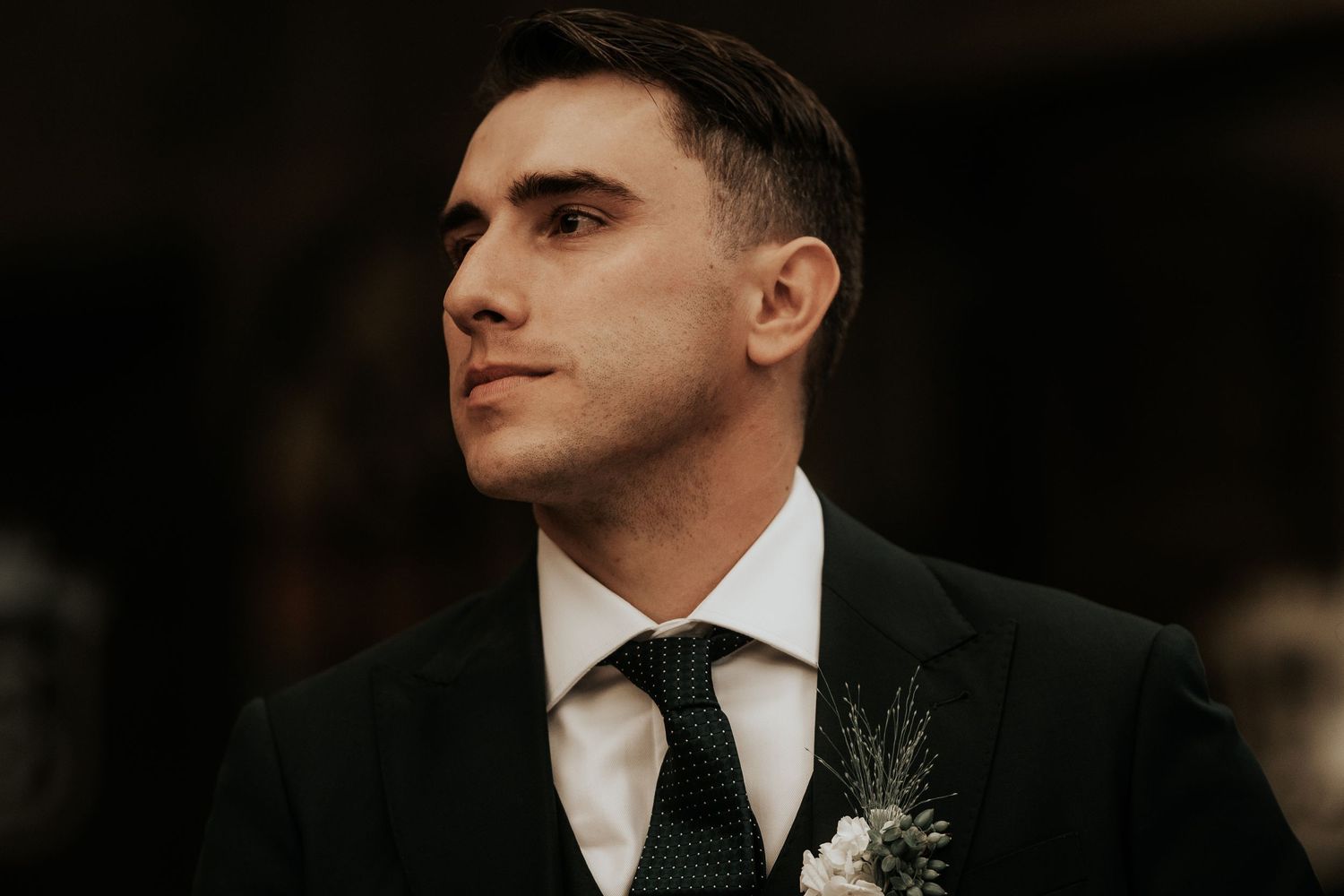 Groom wearing a classic black tuxedo with white boutonniere at a formal event.