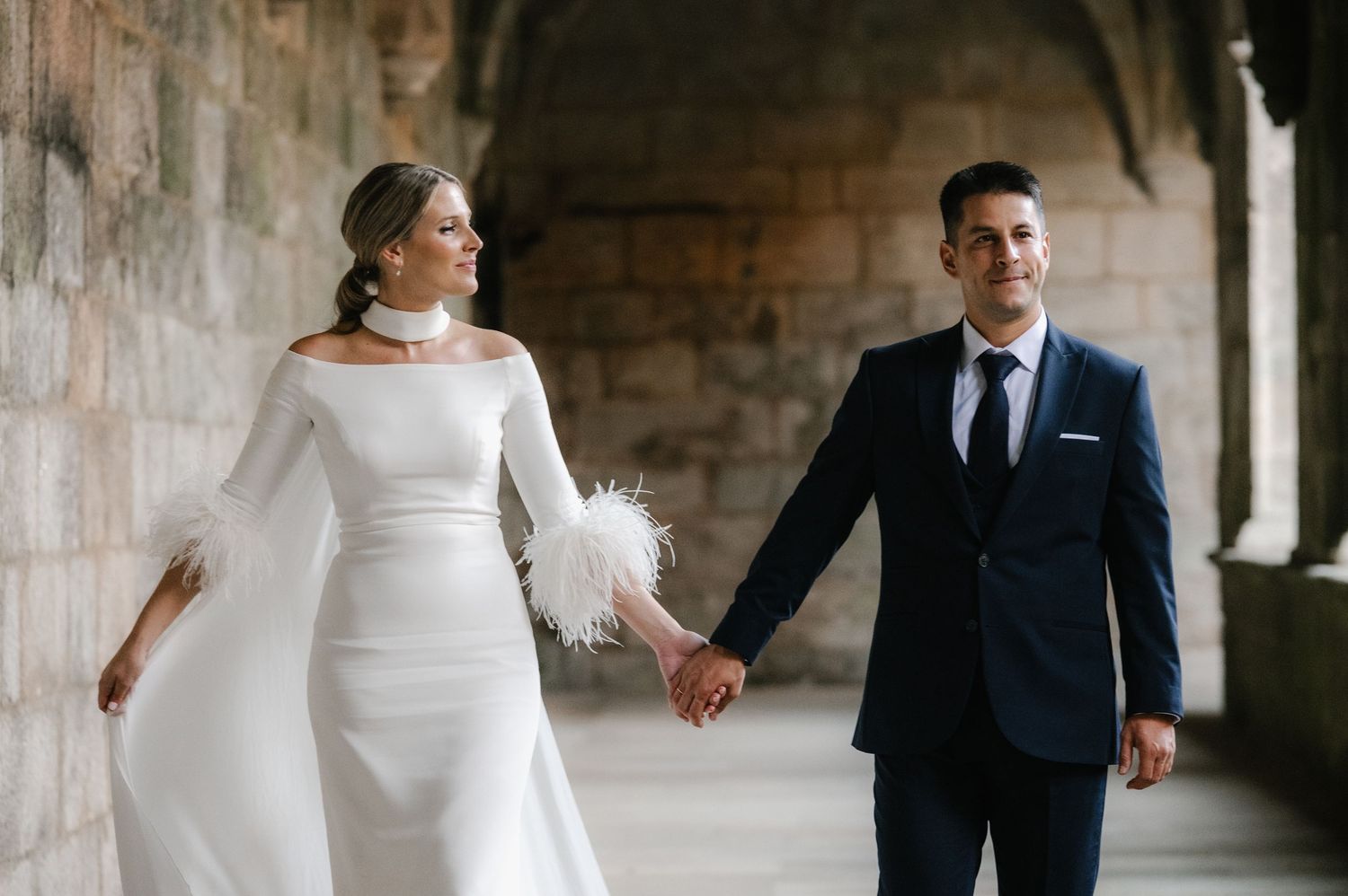 Romantic couple portrait under stone archway in elegant wedding attire.