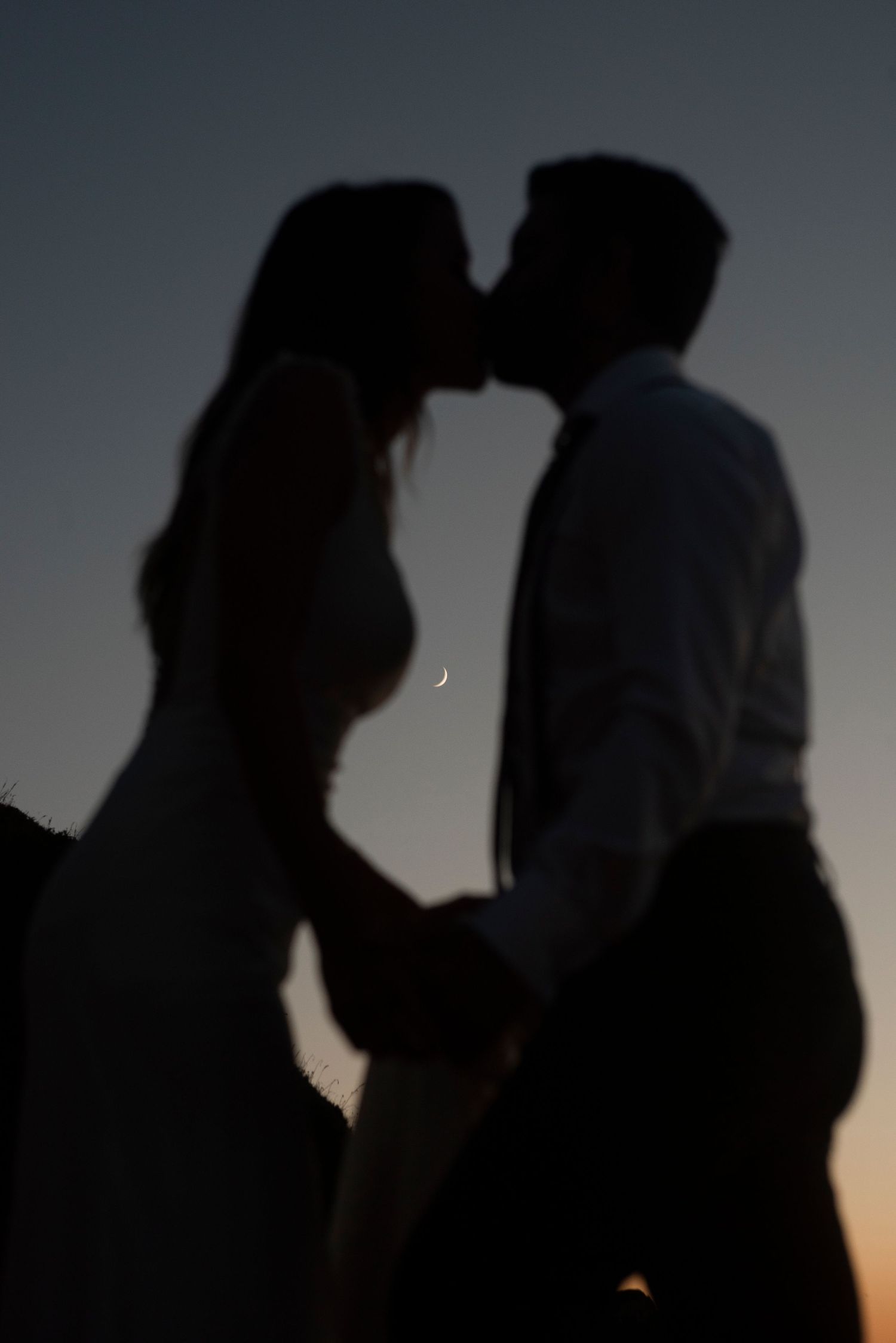 Silhouettes of two people in romantic poses against a dusky sky background with a crescent moon visible.