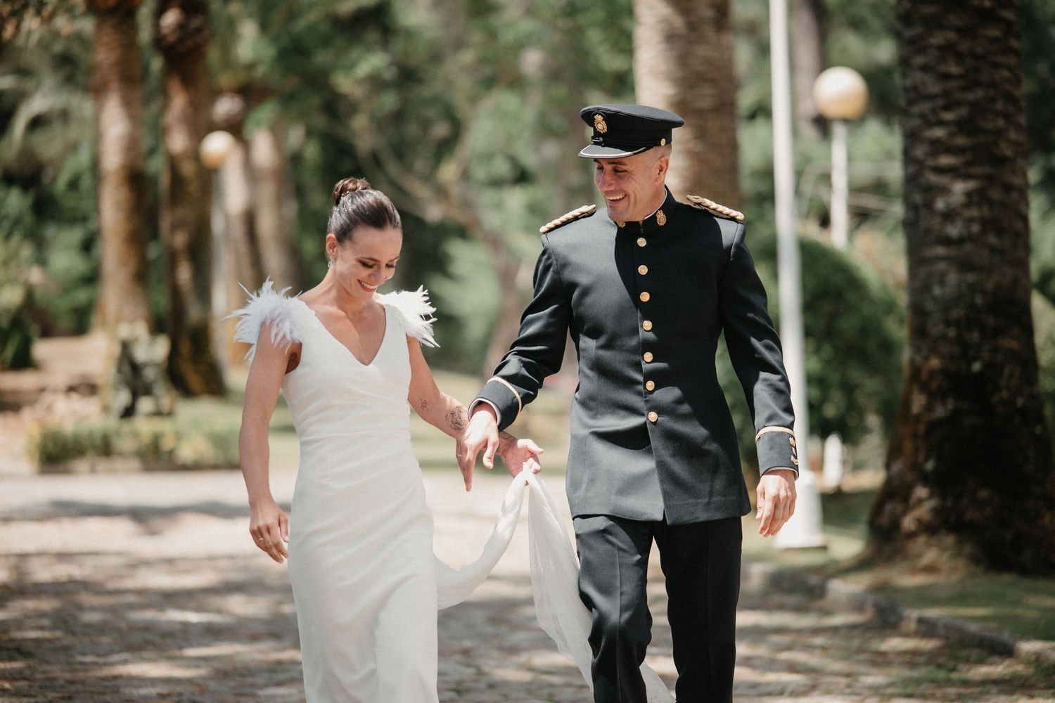 A couple in wedding attire walks through a lush garden path during an outdoor wedding ceremony.
