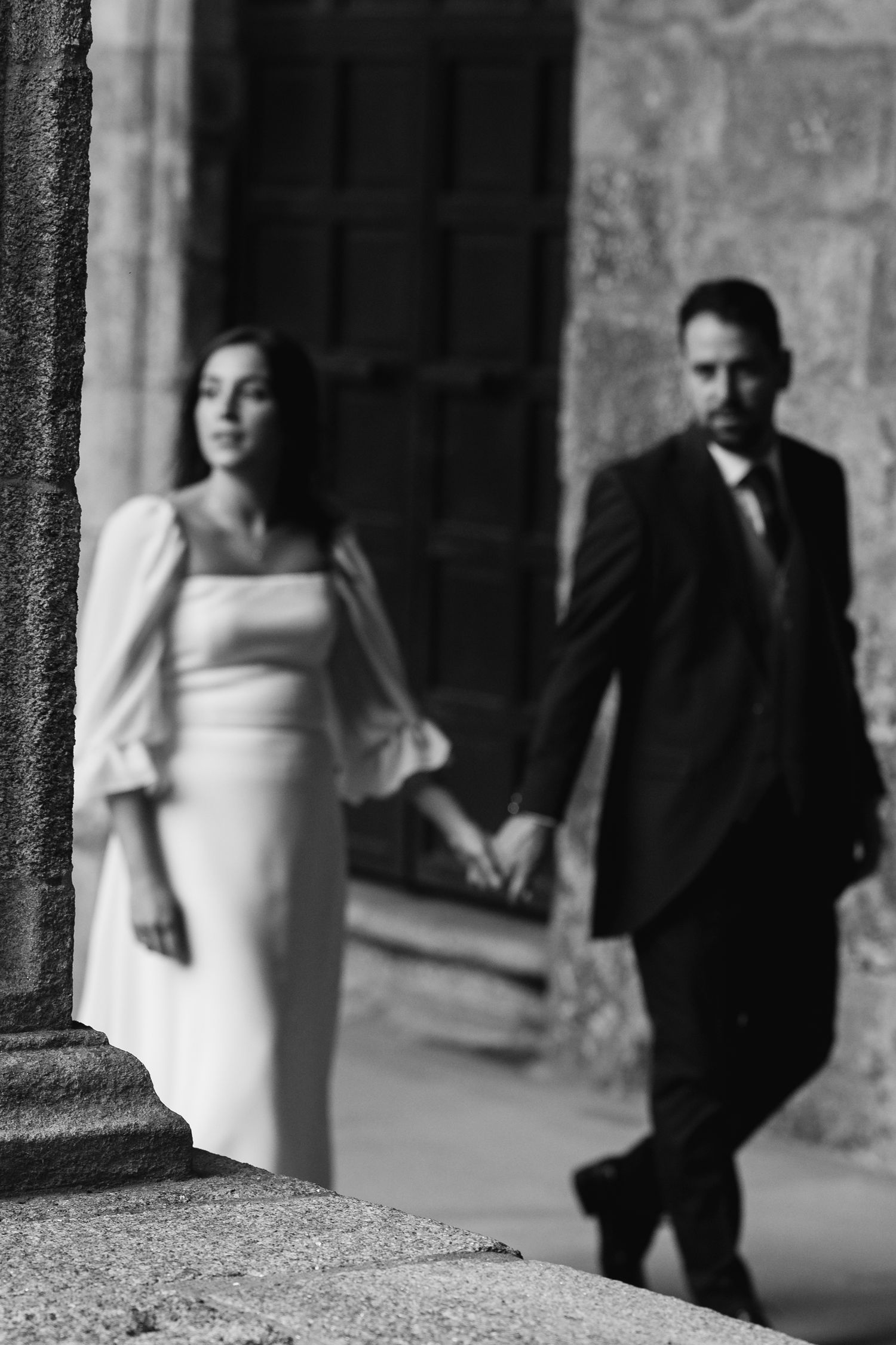 A black and white wedding photo sequence showing a couple walking through a stone archway in an artistic blur effect.