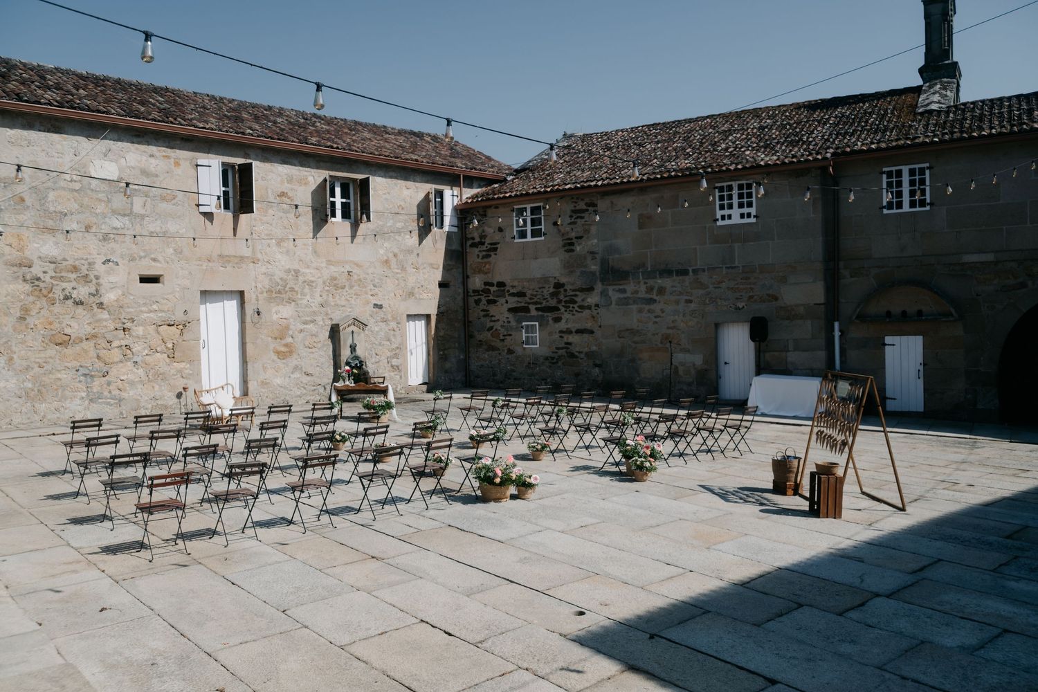 Outdoor wedding ceremony setup with rows of chairs on stone patio surrounded by historic buildings.