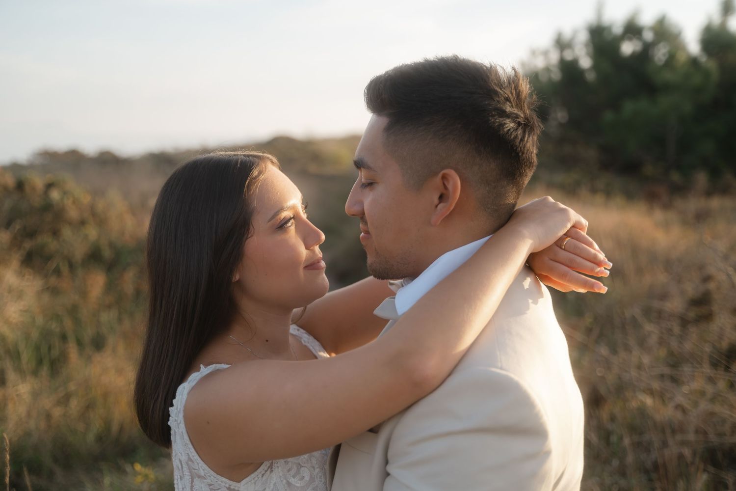 Romantic couple embraces during golden hour sunset photoshoot in a rustic outdoor setting.
