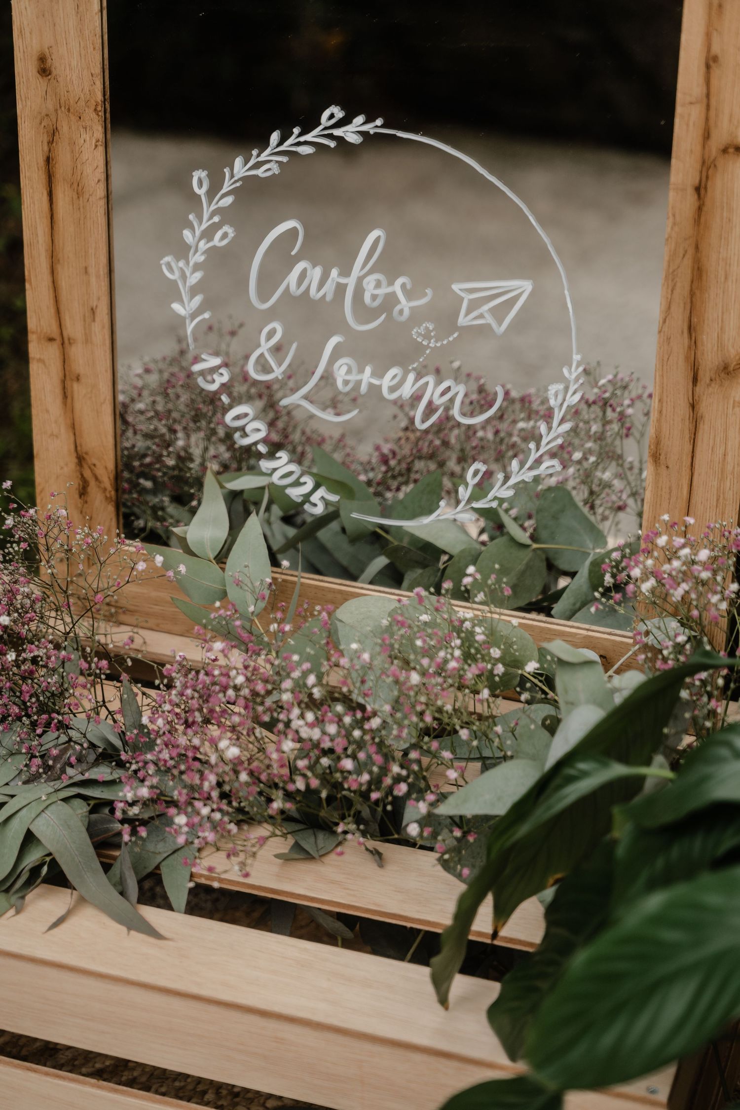 Delicate floral arrangements with greenery and handwritten names displayed in wooden frames for wedding decor.