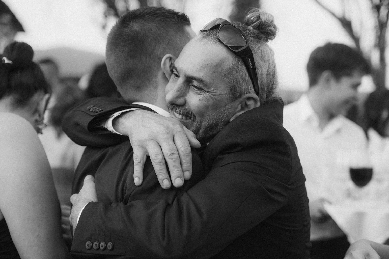 Black and white photo showing emotional embraces between people at what appears to be a celebration or gathering.