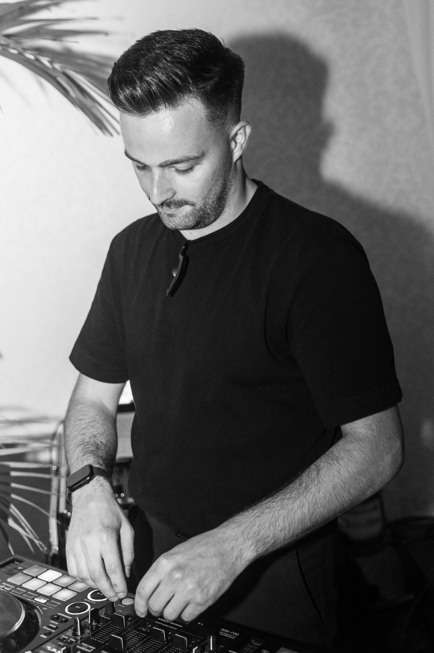 DJ in black t-shirt performing at mixing console in dramatic black and white photography.