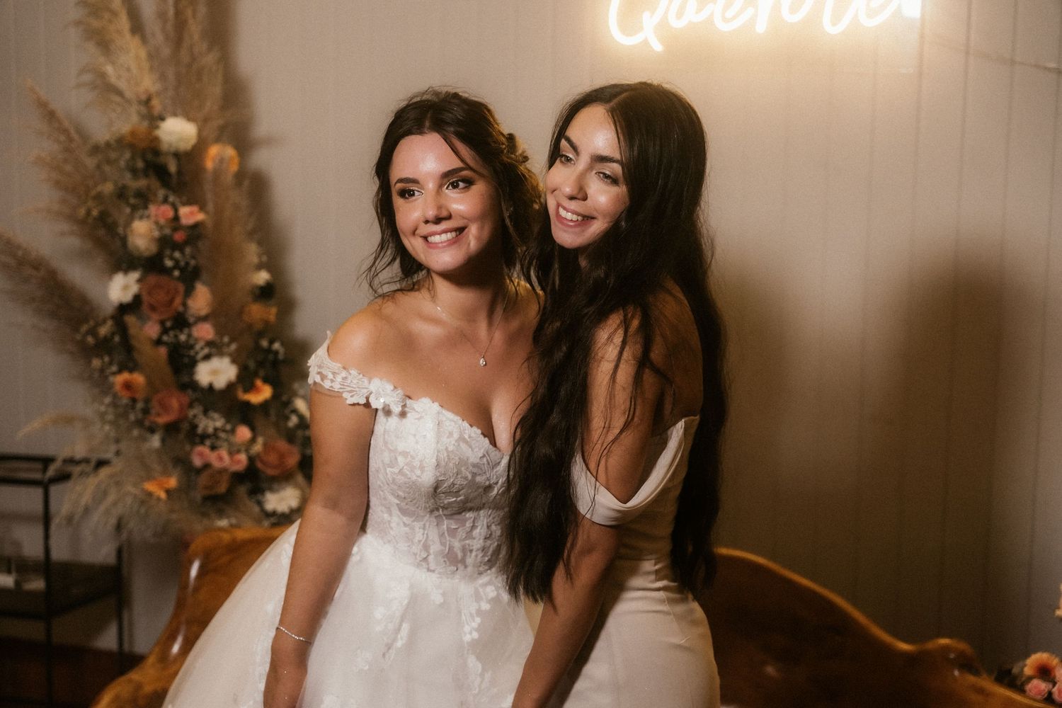 Two people embrace and laugh together at a wedding celebration with floral decorations in the background.
