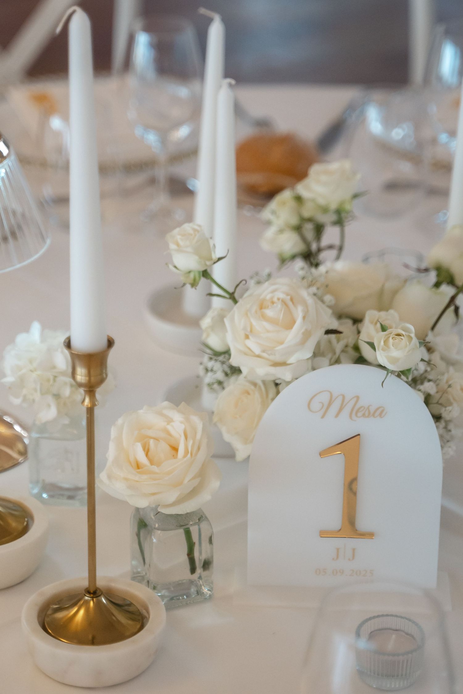 Elegant white roses and gold candle holders decorate a wedding reception table with table number cards.