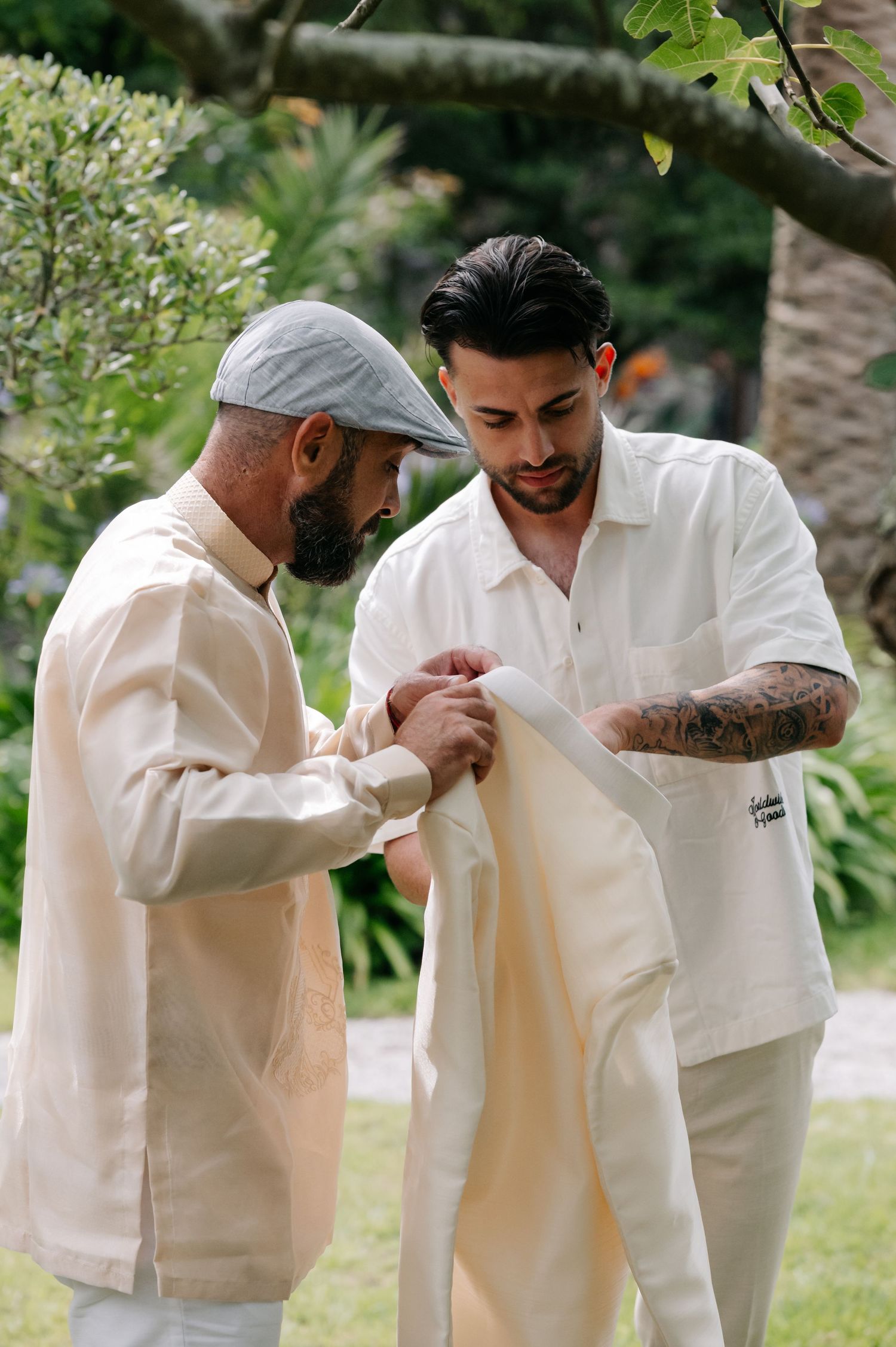 Two people in white clothing share an emotional moment in a garden setting.