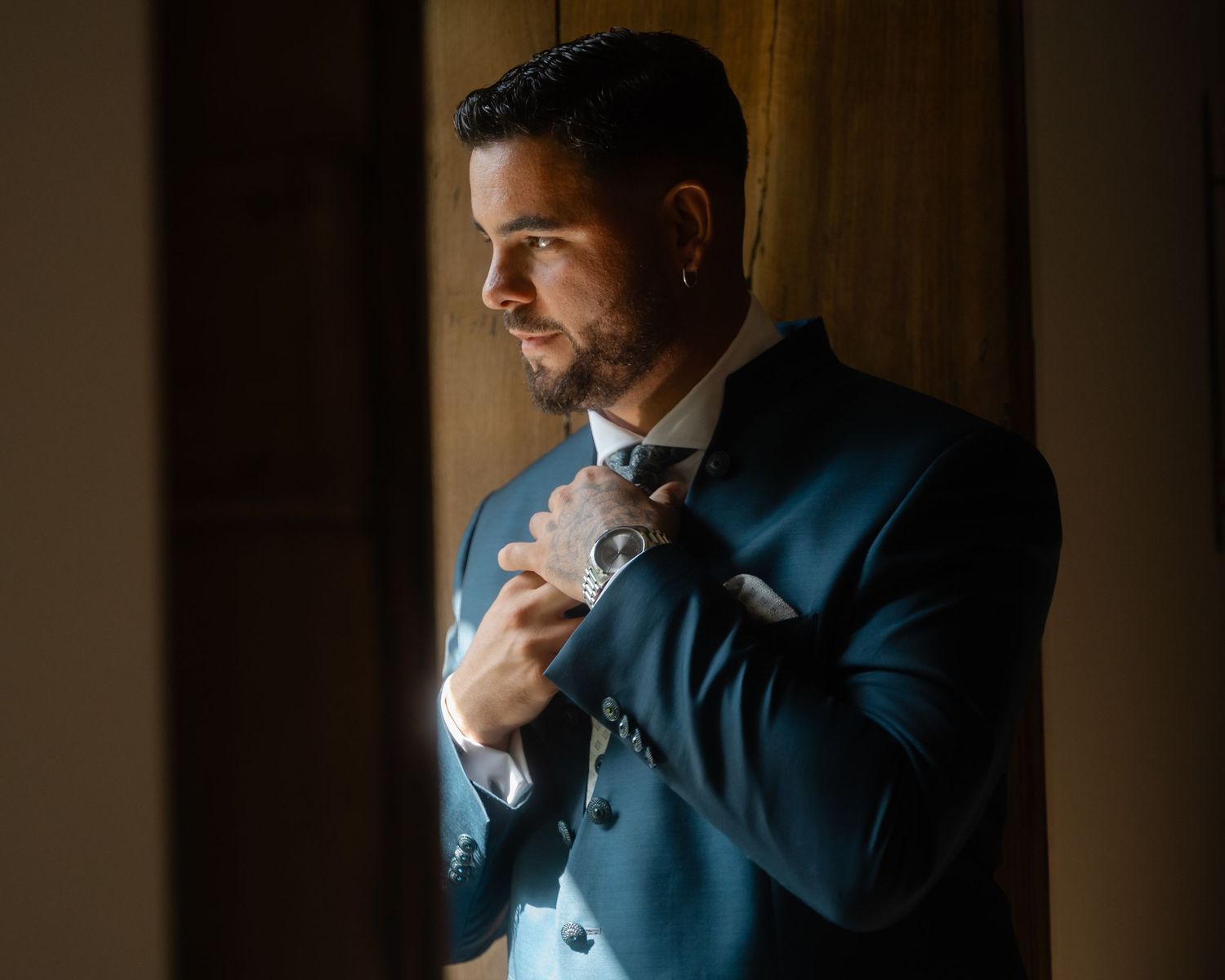 Silhouetted figure in blue suit standing by window in atmospheric dark room.