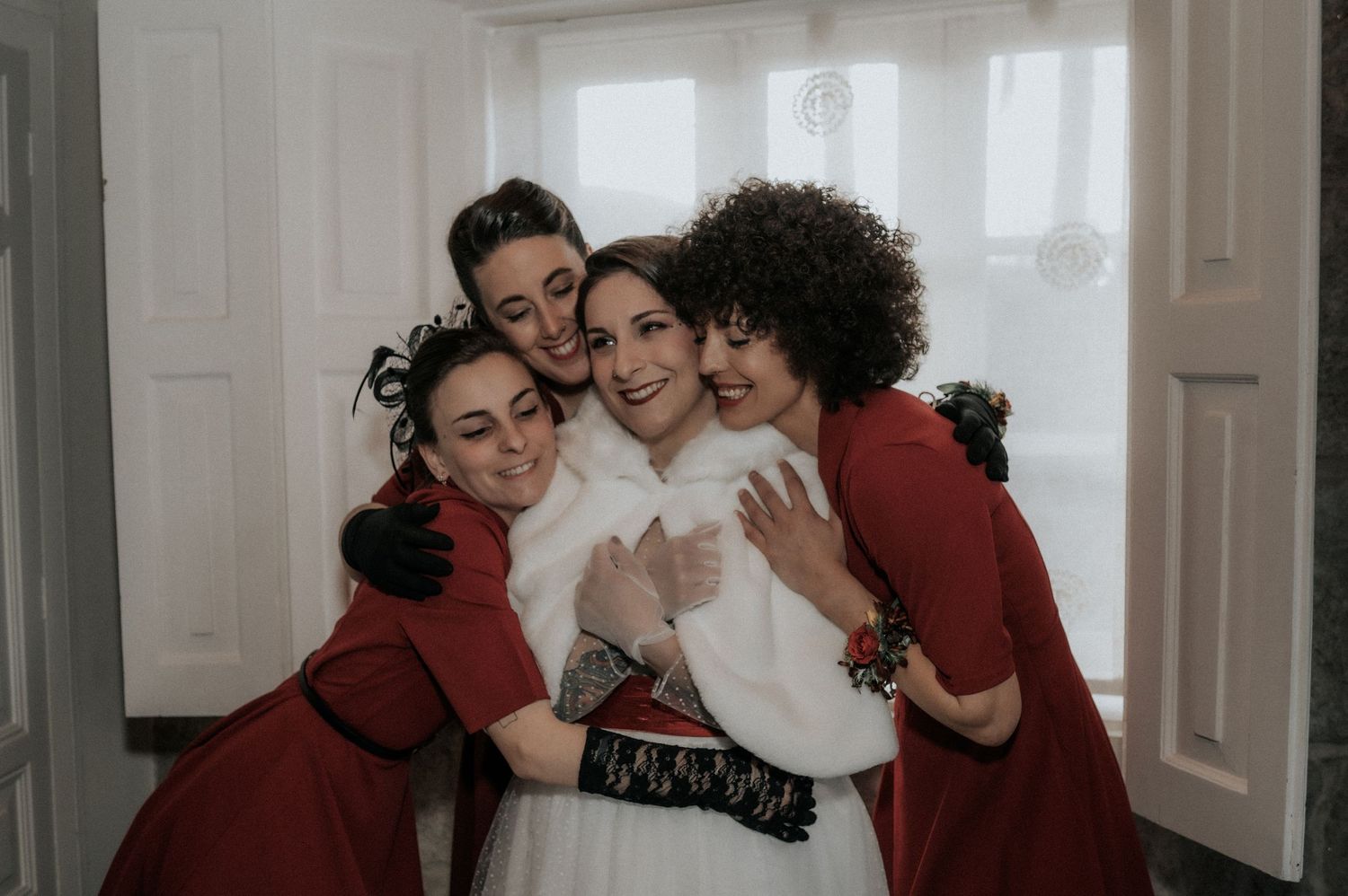 A group of friends embrace in a warm group hug in a bright hallway setting.