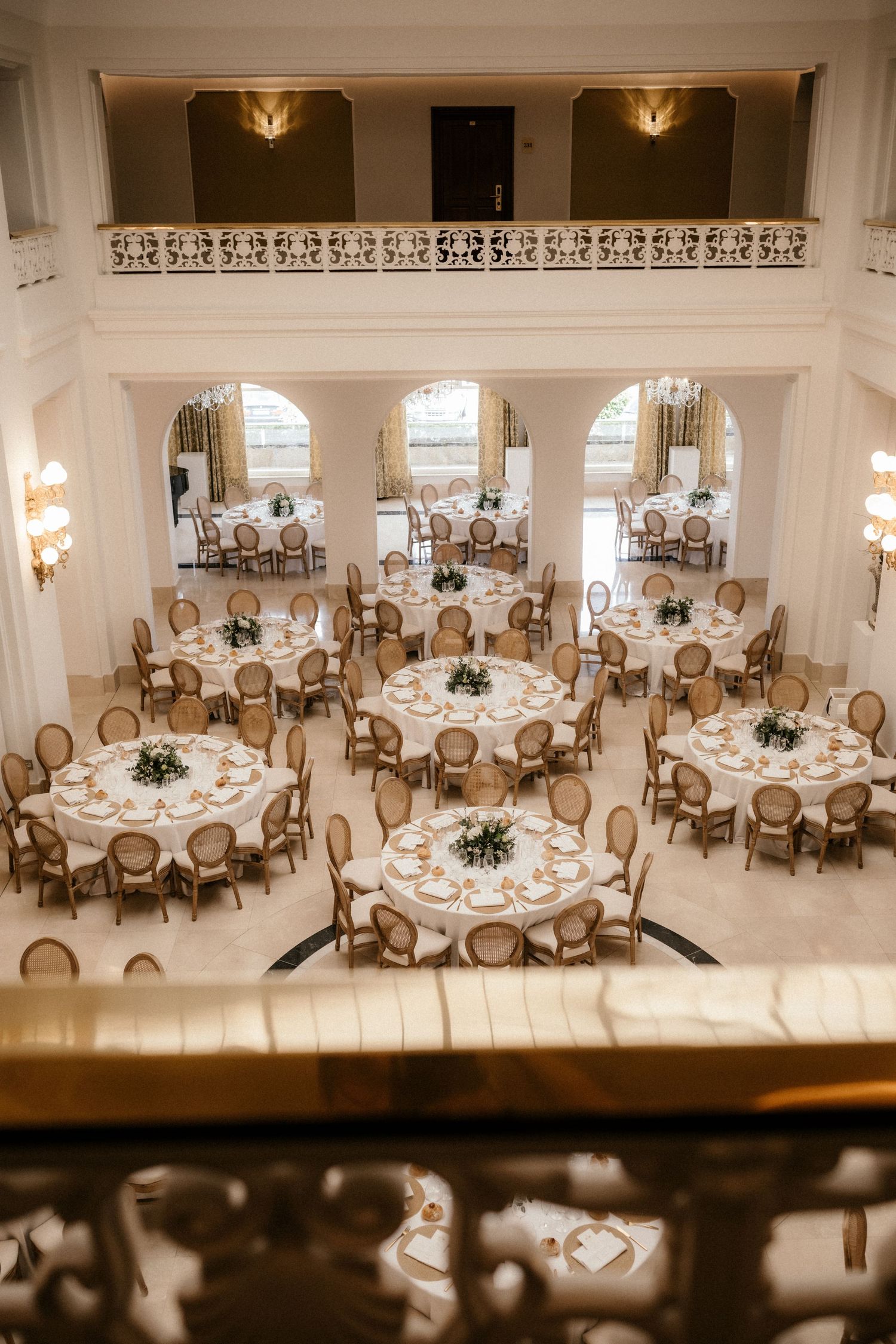 Elegant wedding reception venue with round tables, French-style chairs, and soft lighting in a cream-colored ballroom.