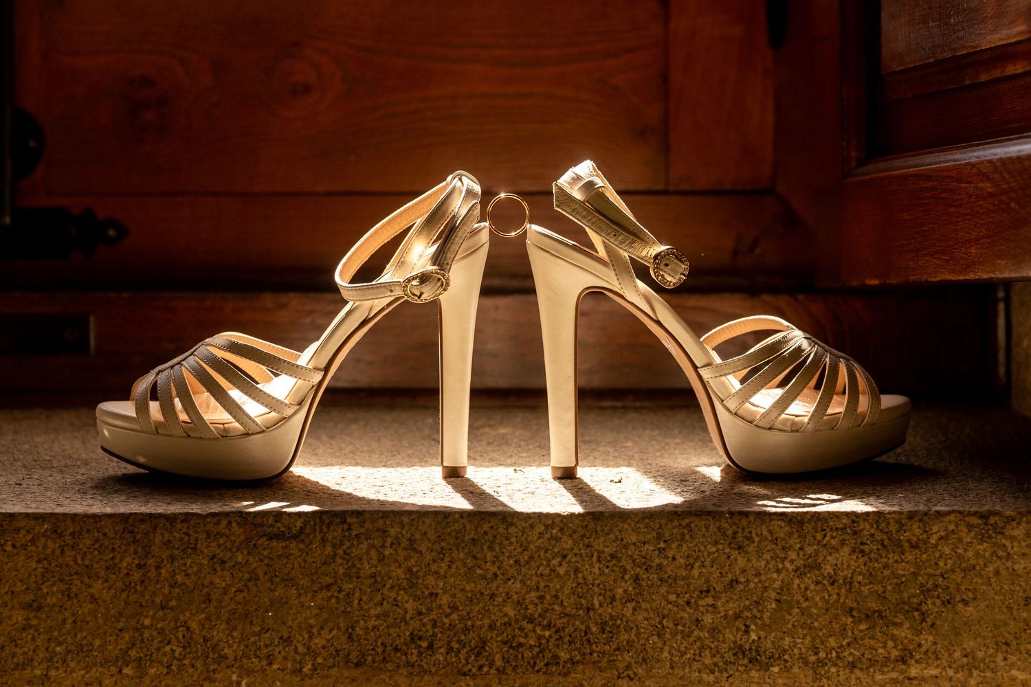Elegant gold strappy high heel sandals illuminated from below creating dramatic shadows on wooden floor.