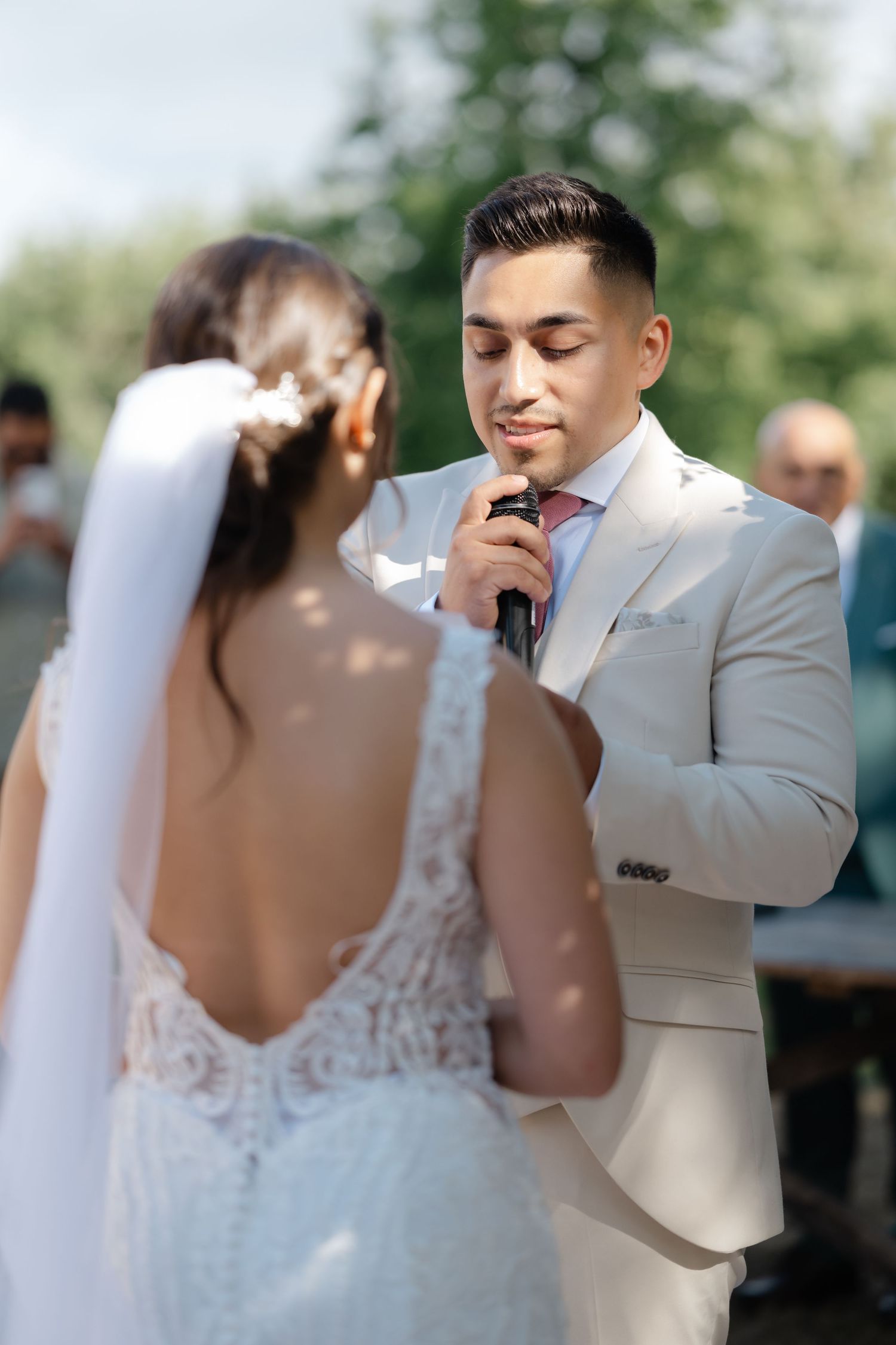 A tender first look moment between a bride in white lace and groom in light gray suit during their outdoor wedding ceremony.