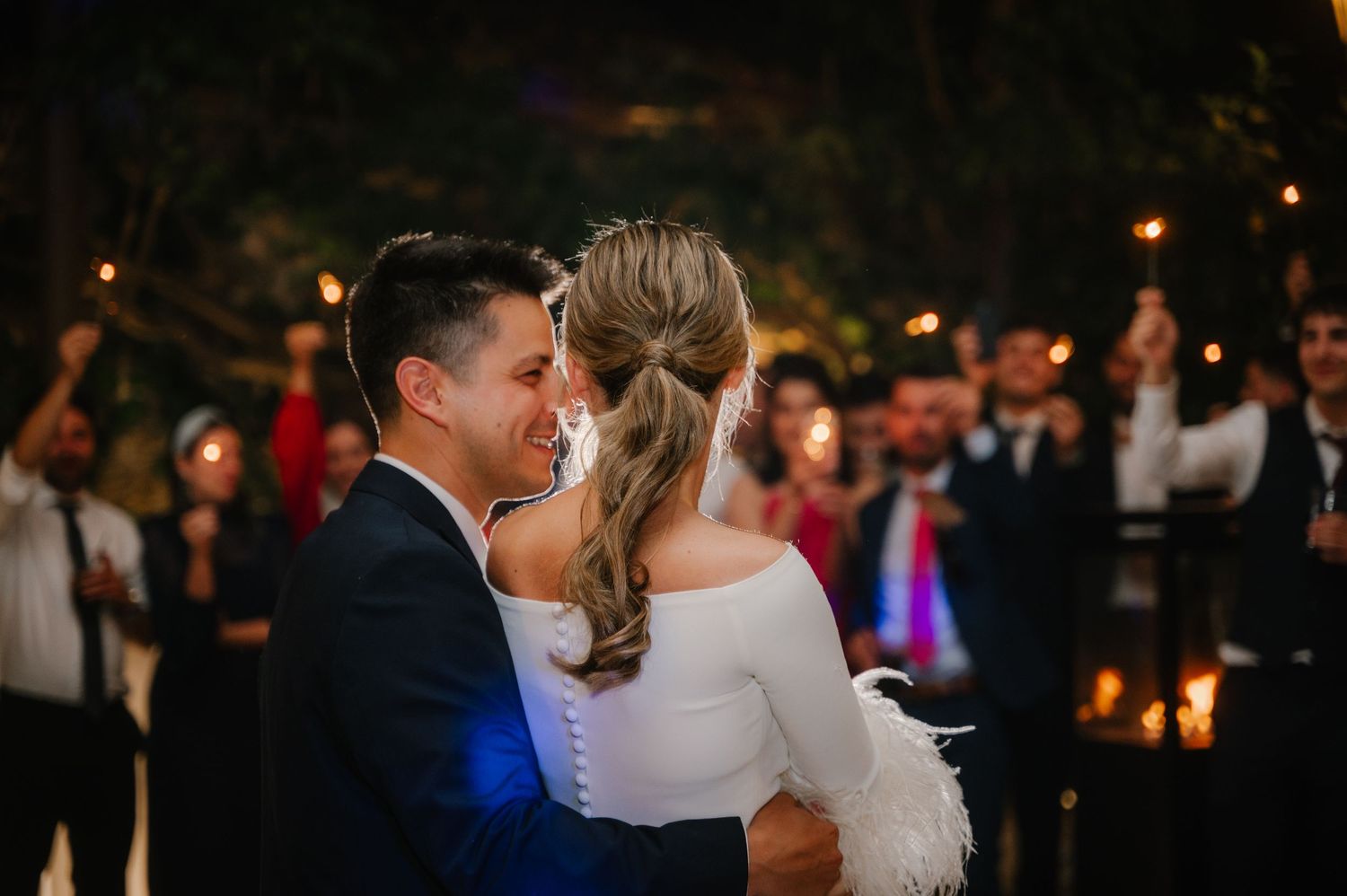 Wedding reception guests dance together on a dimly lit dance floor with warm lighting and festive atmosphere.