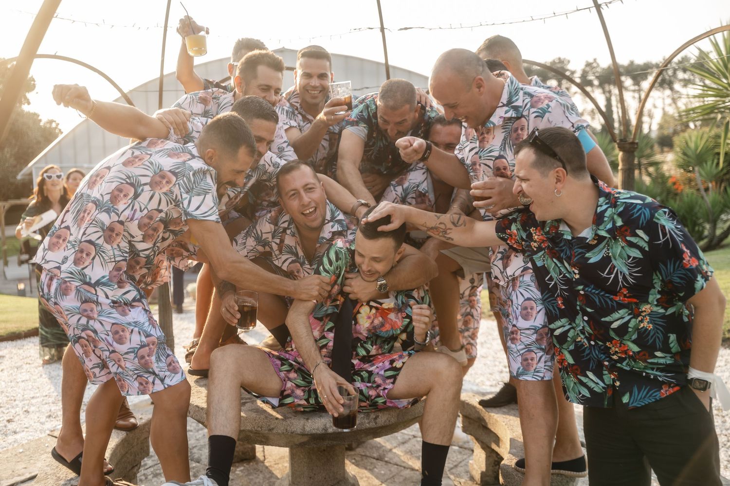 A group of people in floral print shirts gather around and interact with small dogs on a sunny outdoor patio.