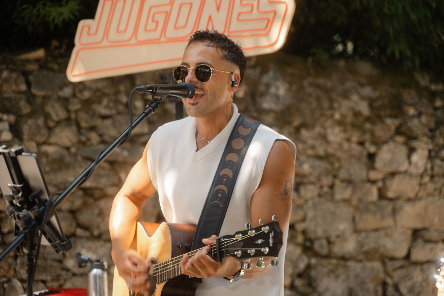 Guitarist plays acoustic music at a rustic outdoor venue with stone wall backdrop.