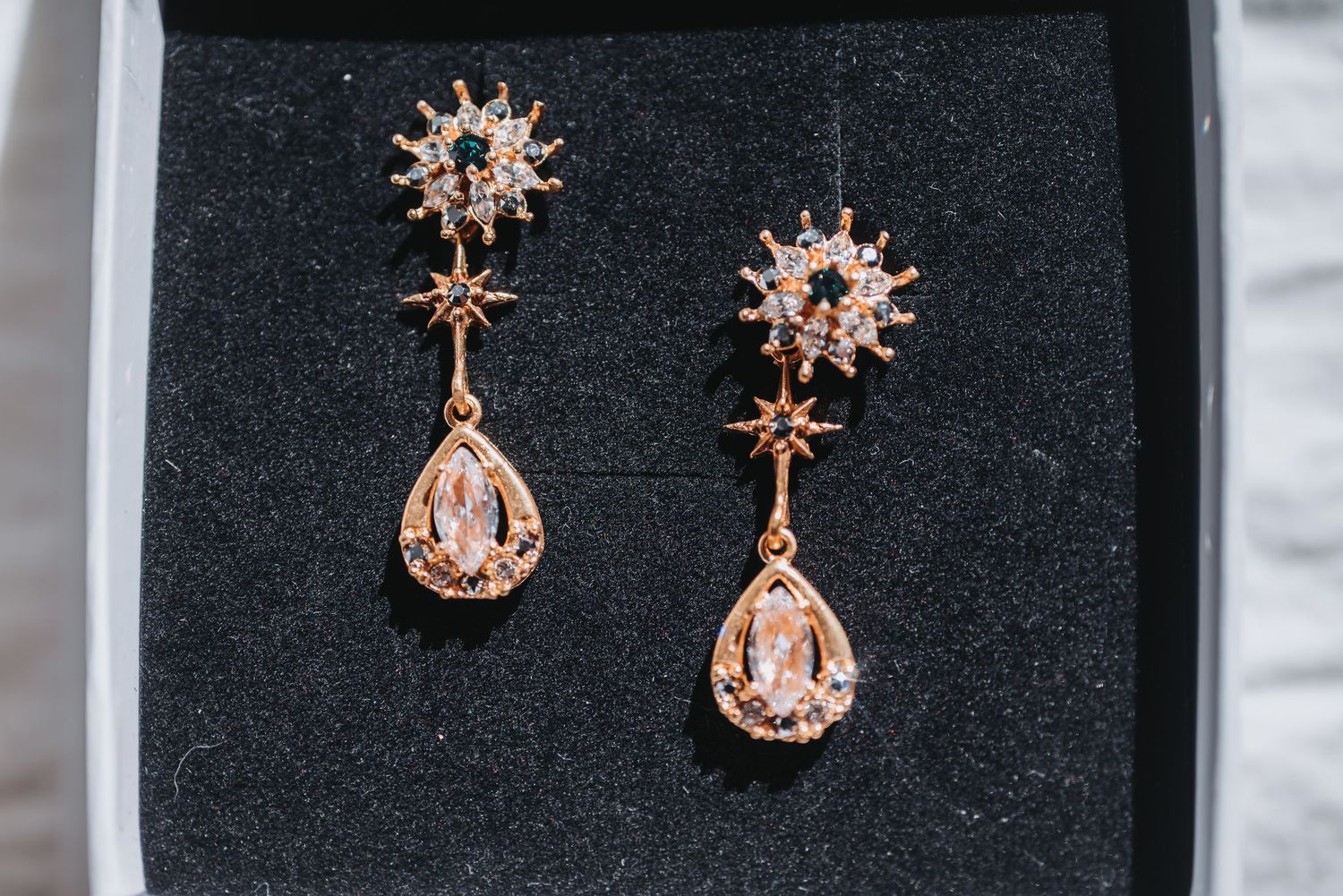 Delicate rose gold jewelry display showing star and crown-shaped earrings against a black velvet background.